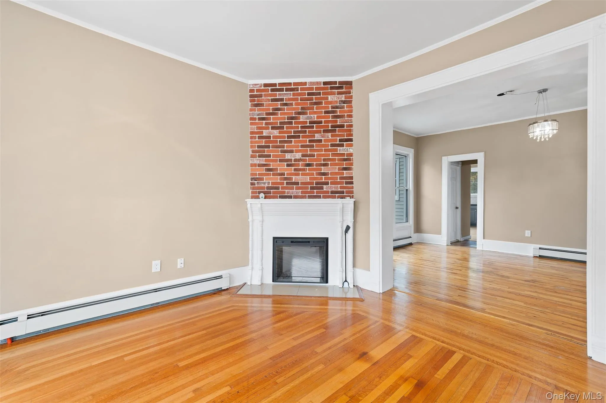 Unfurnished living room featuring light wood-style floors, crown molding, a fireplace with flush hearth, and baseboard heating Unfurnished living room featuring light wood-style floors, crown molding, a fireplace with flush hearth, and baseboard heating