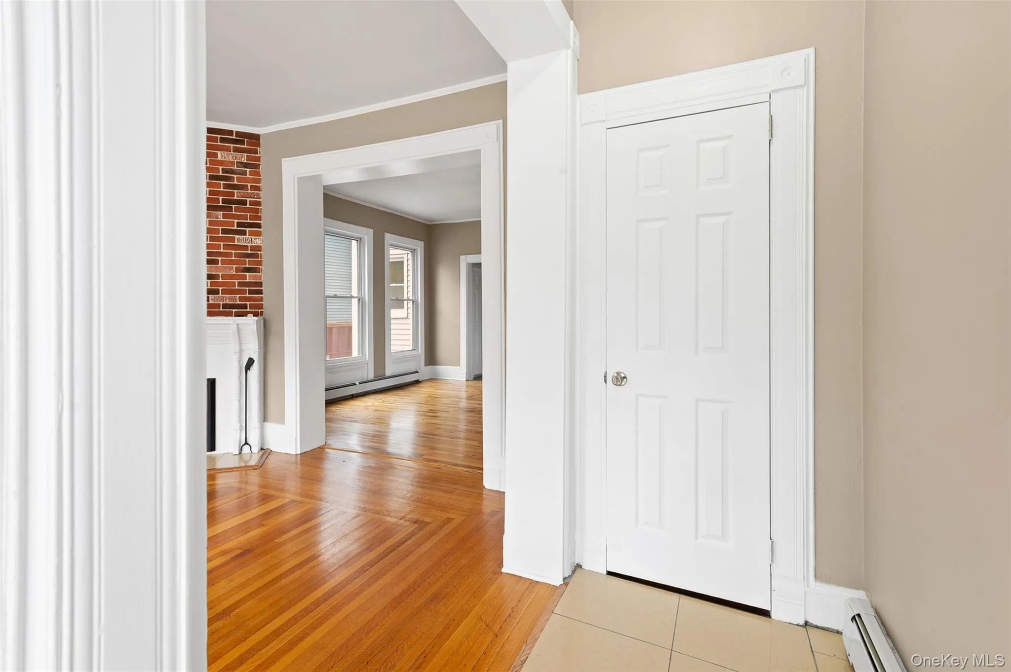 Hallway with a baseboard heating unit, ornamental molding, and light wood-type flooring Hallway with a baseboard heating unit, ornamental molding, and light wood-type flooring