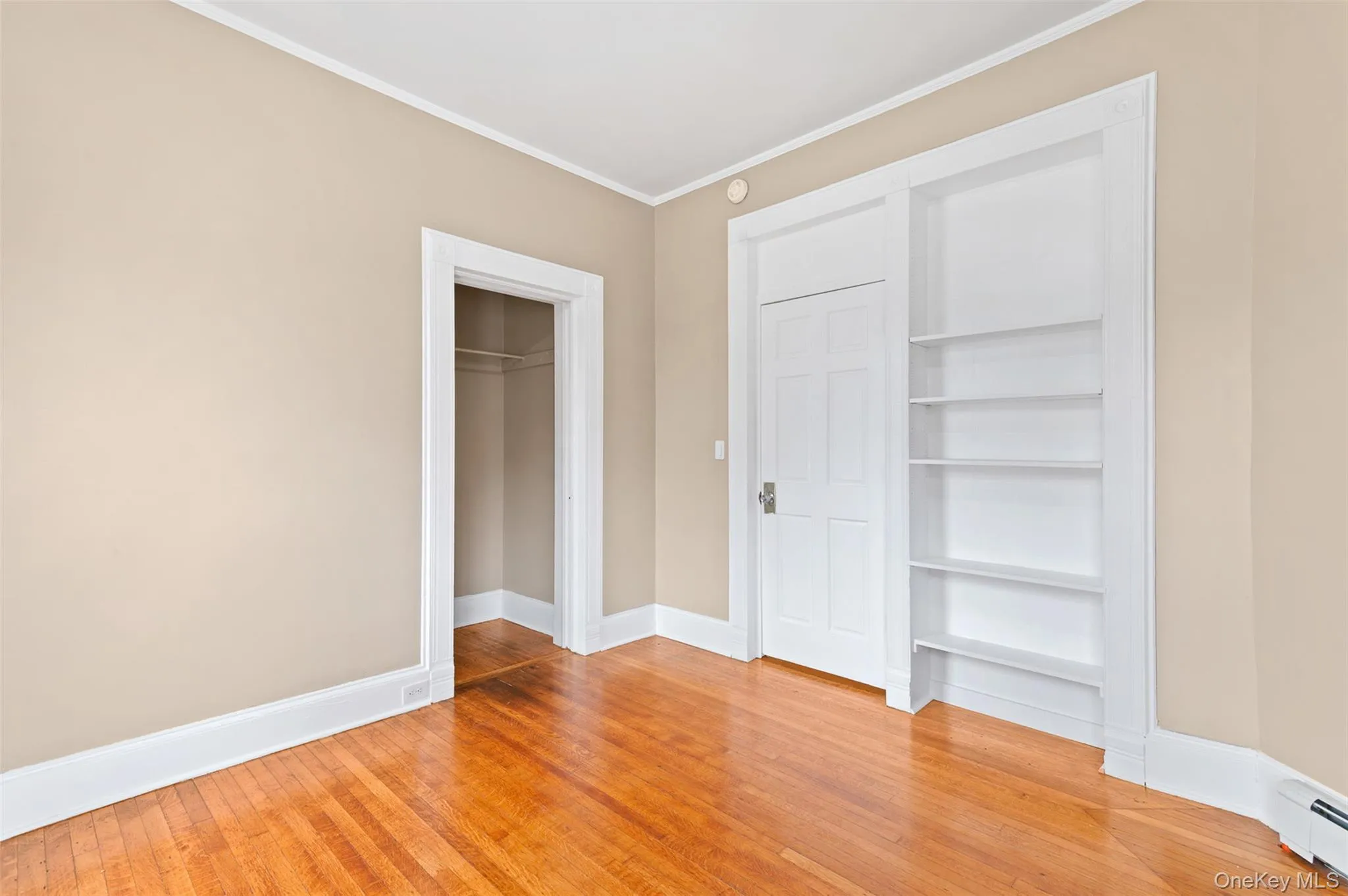 Unfurnished bedroom featuring light wood finished floors, crown molding, a baseboard radiator, and a closet Unfurnished bedroom featuring light wood finished floors, crown molding, a baseboard radiator, and a closet
