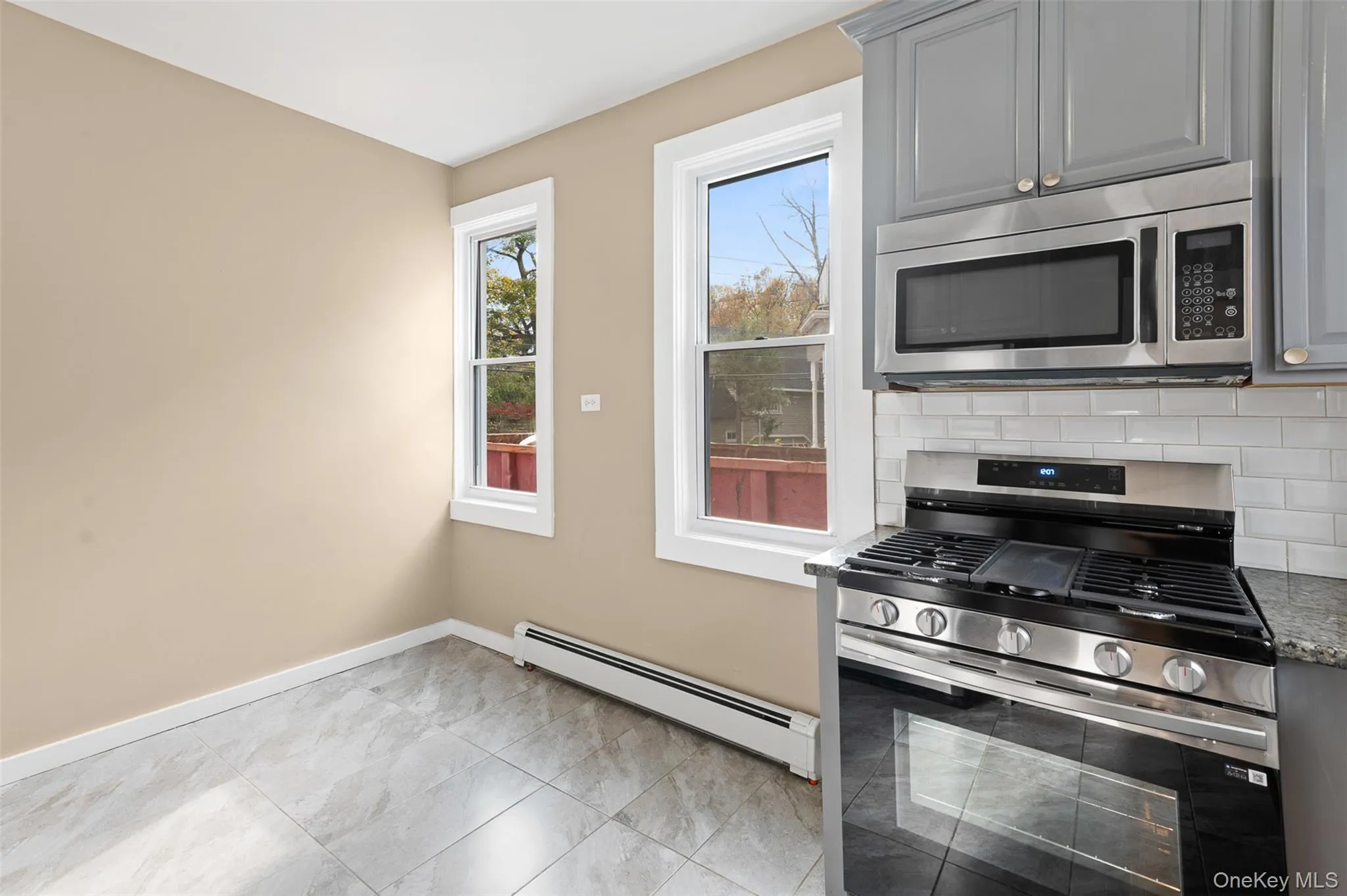 Kitchen featuring stainless steel appliances, a baseboard heating unit, gray cabinets, and light stone countertops Kitchen featuring stainless steel appliances, a baseboard heating unit, gray cabinets, and light stone countertops