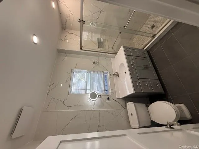Bathroom with tile walls, a marble finish shower, vanity, and dark tile patterned floors Bathroom with tile walls, a marble finish shower, vanity, and dark tile patterned floors