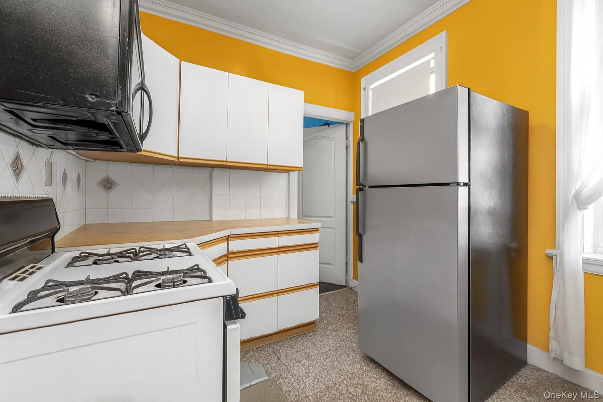 Kitchen featuring white cabinets, gas range gas stove, black microwave, freestanding refrigerator, and ornamental molding Kitchen featuring white cabinets, gas range gas stove, black microwave, freestanding refrigerator, and ornamental molding