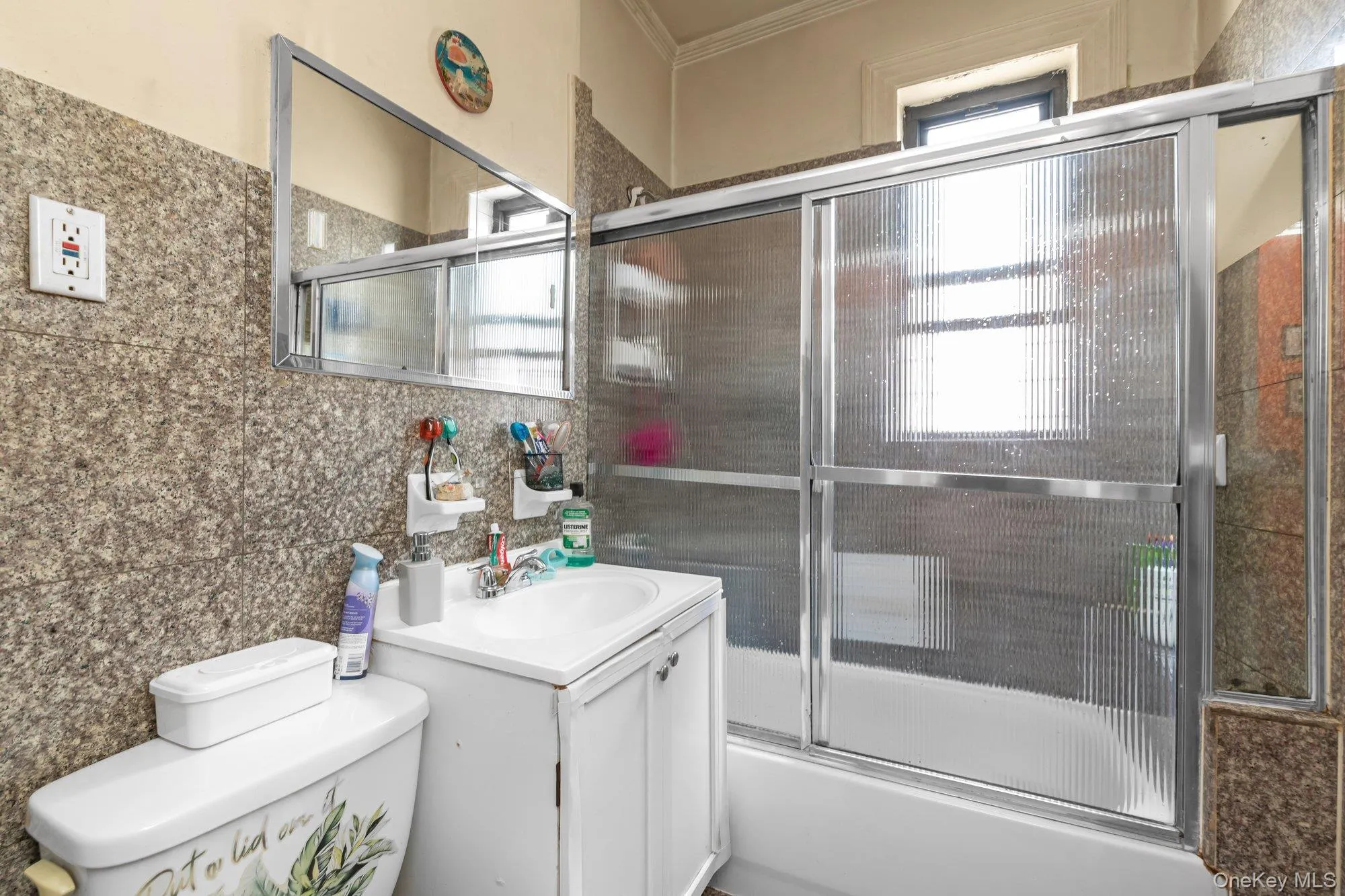 Bathroom featuring vanity, combined bath / shower with glass door, tile walls, backsplash, and ornamental molding Bathroom featuring vanity, combined bath / shower with glass door, tile walls, backsplash, and ornamental molding