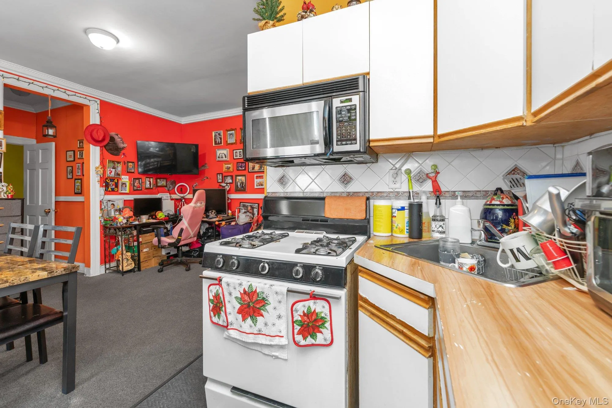 Kitchen with white cabinetry, white gas range oven, light countertops, stainless steel microwave, and a desk Kitchen with white cabinetry, white gas range oven, light countertops, stainless steel microwave, and a desk