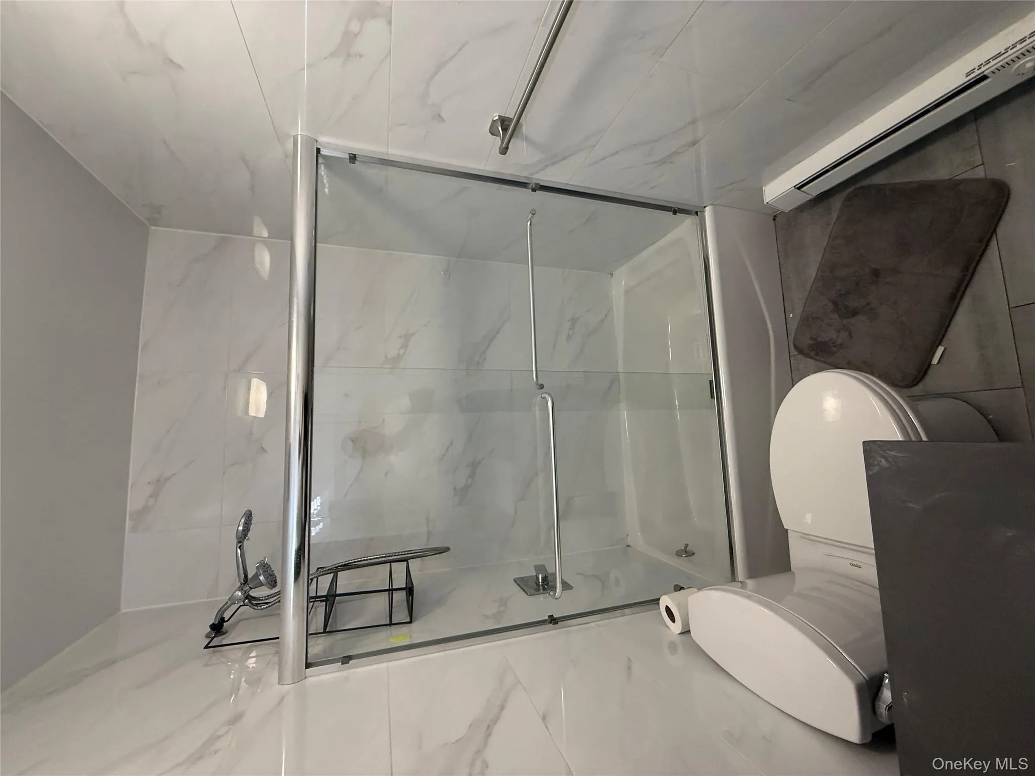 Full bath with a baseboard heating unit, tile walls, shower / bath combination with glass door, and tile patterned floors Full bath with a baseboard heating unit, tile walls, shower / bath combination with glass door, and tile patterned floors