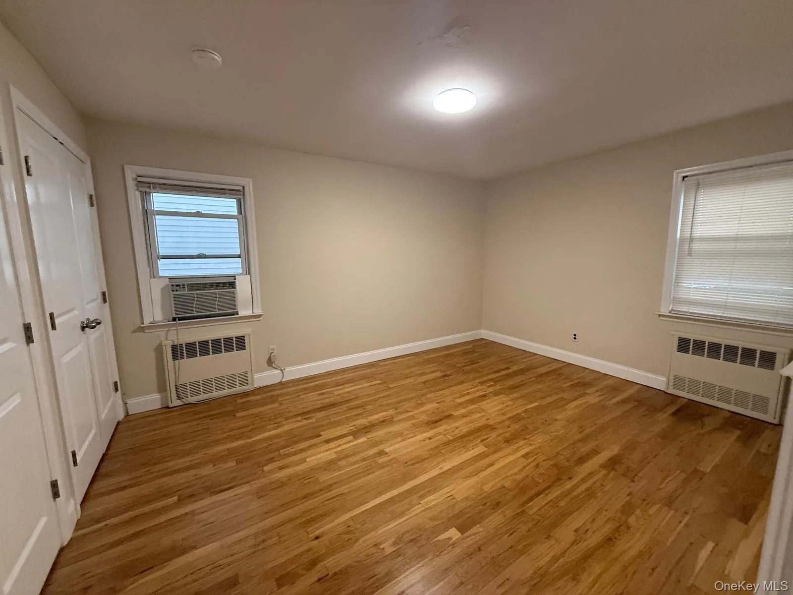 Unfurnished room with light wood-type flooring, radiator heating unit, and plenty of natural light Unfurnished room with light wood-type flooring, radiator heating unit, and plenty of natural light