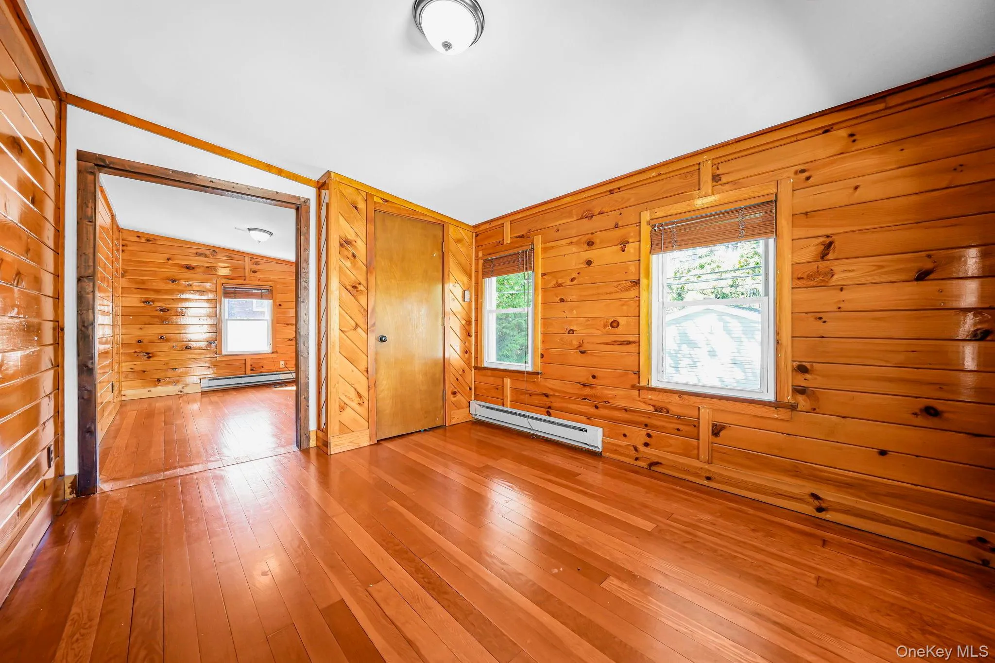 Unfurnished bedroom with hardwood / wood-style floors, baseboard heating, wooden walls, and lofted ceiling Unfurnished bedroom with hardwood / wood-style floors, baseboard heating, wooden walls, and lofted ceiling
