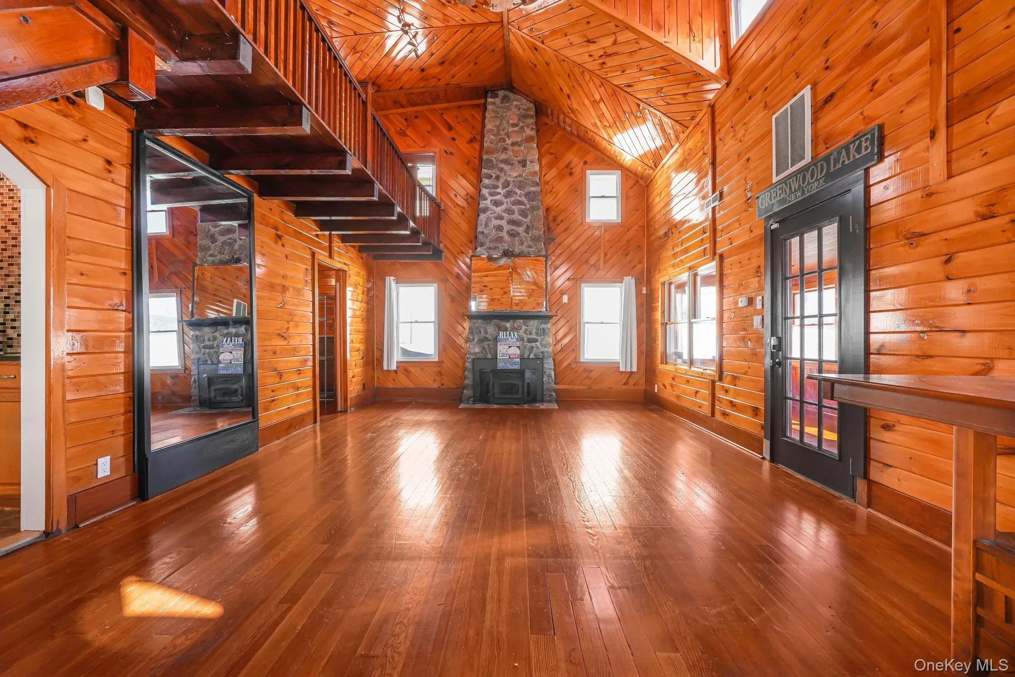 Unfurnished living room with wooden walls, a wood stove, wood-type flooring, high vaulted ceiling, and wood ceiling Unfurnished living room with wooden walls, a wood stove, wood-type flooring, high vaulted ceiling, and wood ceiling
