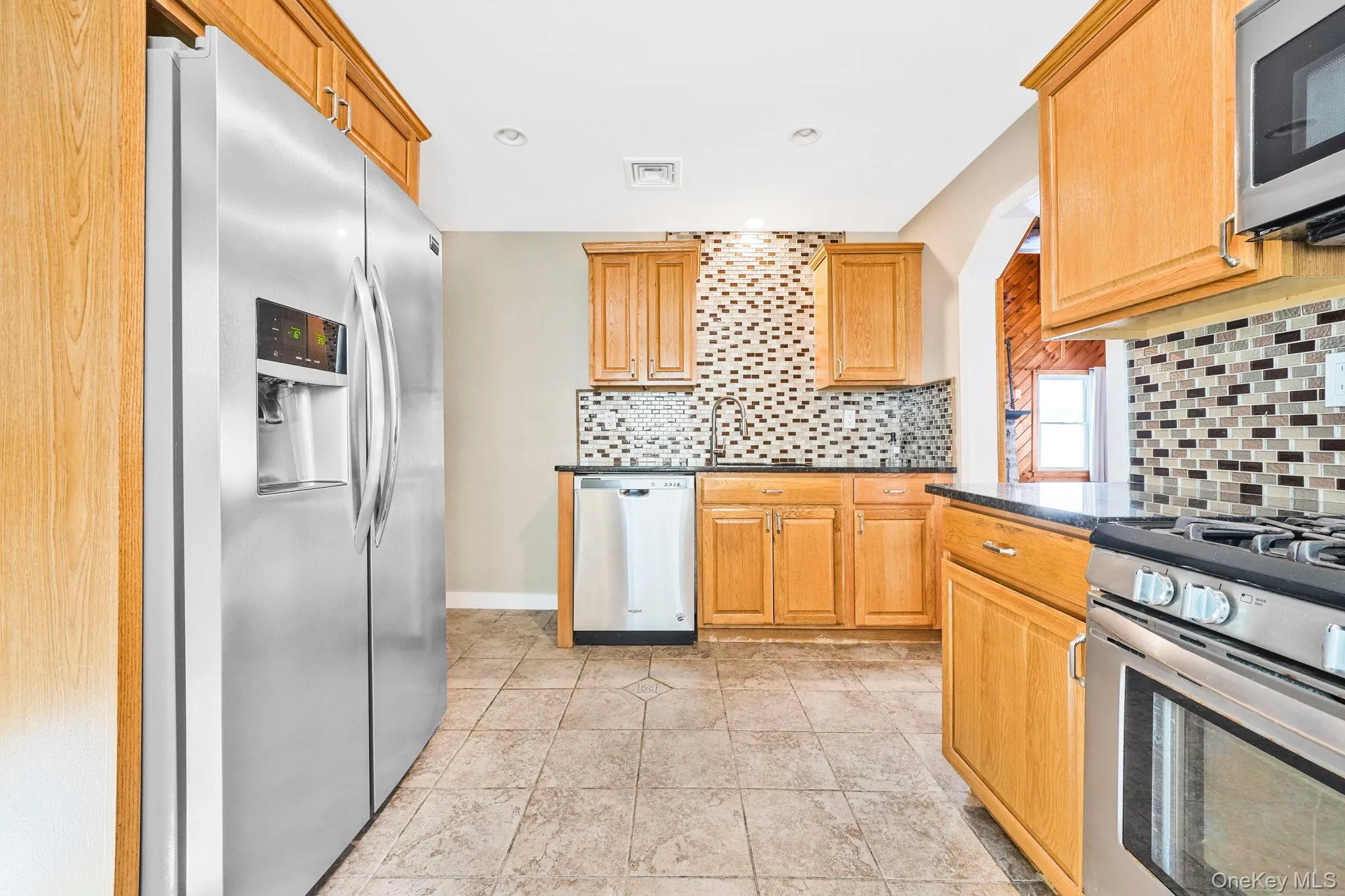 Kitchen with stainless steel appliances, decorative backsplash, light tile patterned floors, dark stone counters, and recessed lighting Kitchen with stainless steel appliances, decorative backsplash, light tile patterned floors, dark stone counters, and recessed lighting