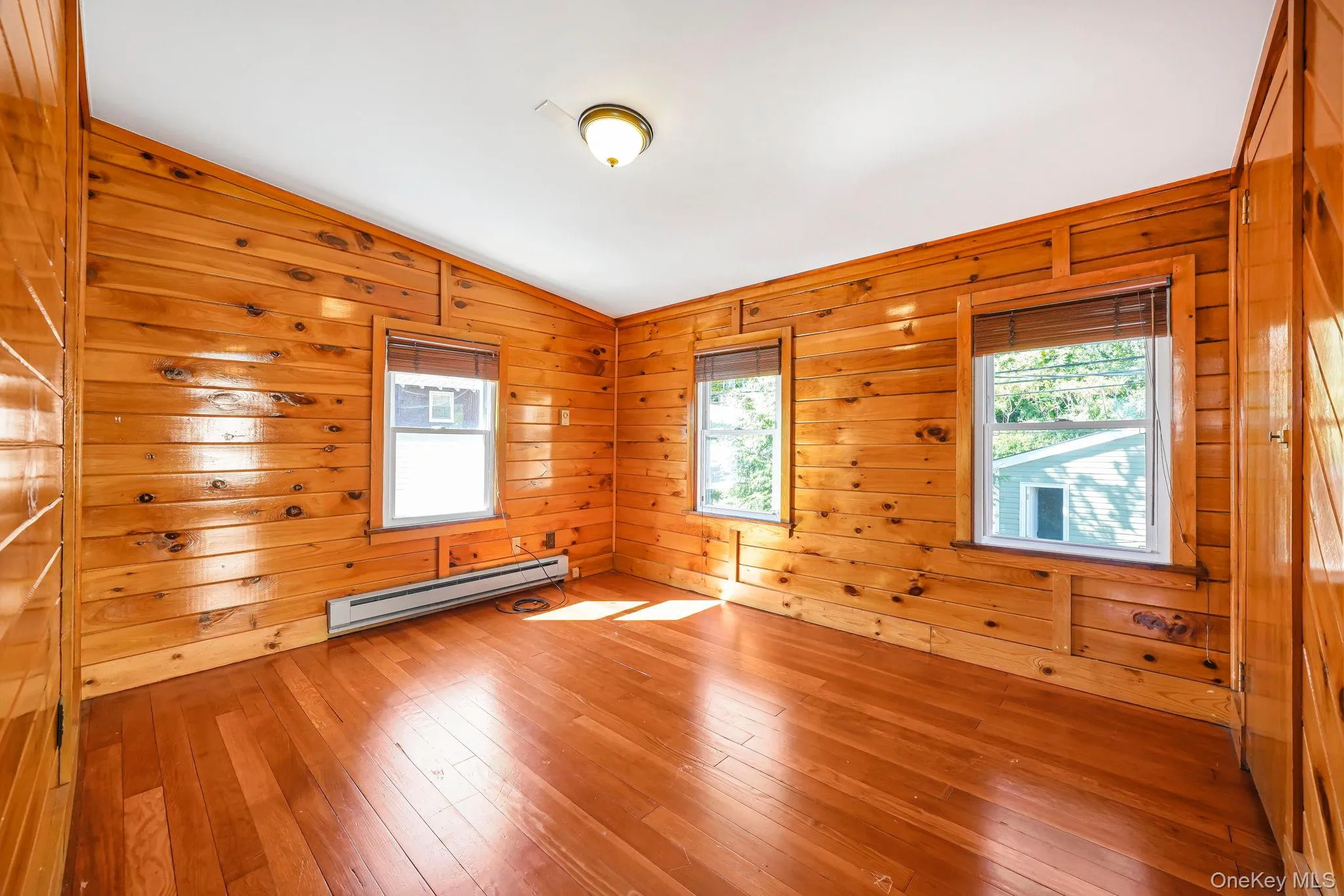 Empty room featuring wooden walls, lofted ceiling, hardwood / wood-style floors, healthy amount of natural light, and a baseboard radiator Empty room featuring wooden walls, lofted ceiling, hardwood / wood-style floors, healthy amount of natural light, and a baseboard radiator