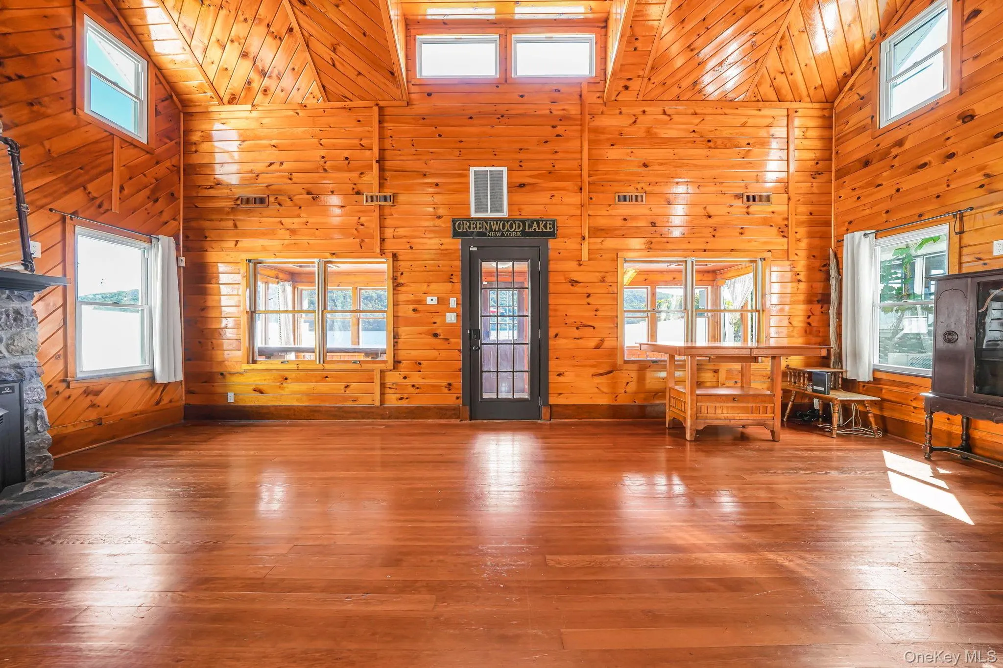 Unfurnished living room featuring a high ceiling, wood walls, and hardwood / wood-style floors Unfurnished living room featuring a high ceiling, wood walls, and hardwood / wood-style floors