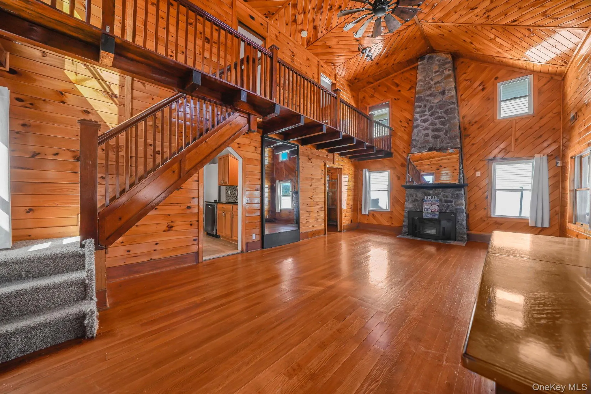 Unfurnished living room featuring wooden walls, wood ceiling, a wood stove, stairway, and ceiling fan Unfurnished living room featuring wooden walls, wood ceiling, a wood stove, stairway, and ceiling fan