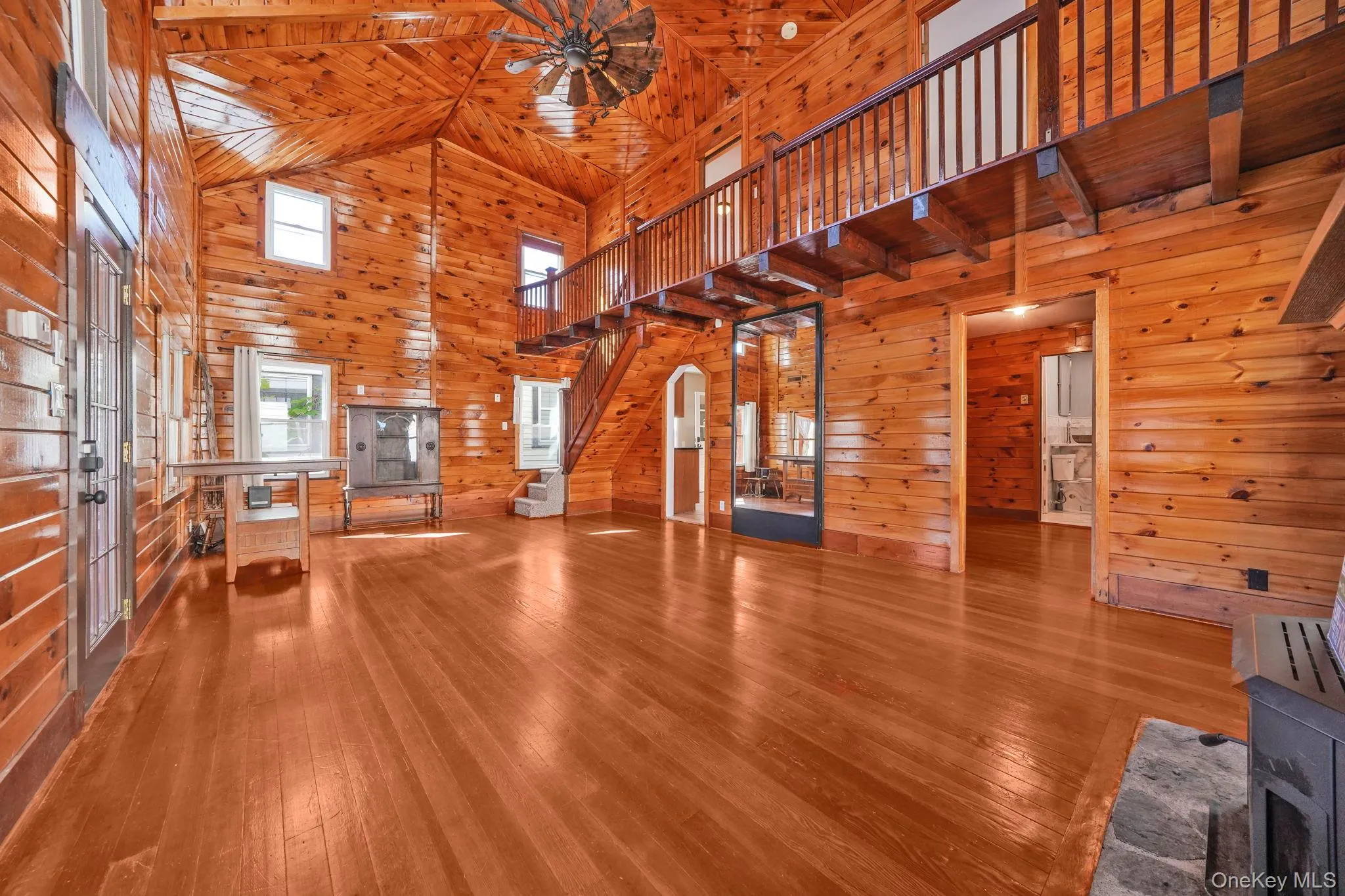 Unfurnished living room featuring wooden walls, high vaulted ceiling, wooden ceiling, hardwood / wood-style floors, and stairway Unfurnished living room featuring wooden walls, high vaulted ceiling, wooden ceiling, hardwood / wood-style floors, and stairway