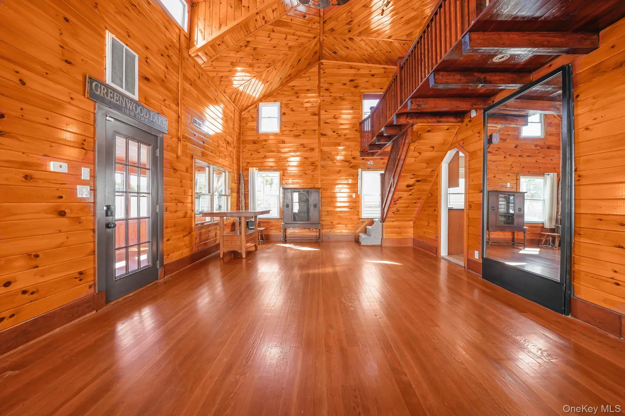 Unfurnished living room featuring stairs, wooden walls, hardwood / wood-style flooring, high vaulted ceiling, and wood ceiling Unfurnished living room featuring stairs, wooden walls, hardwood / wood-style flooring, high vaulted ceiling, and wood ceiling