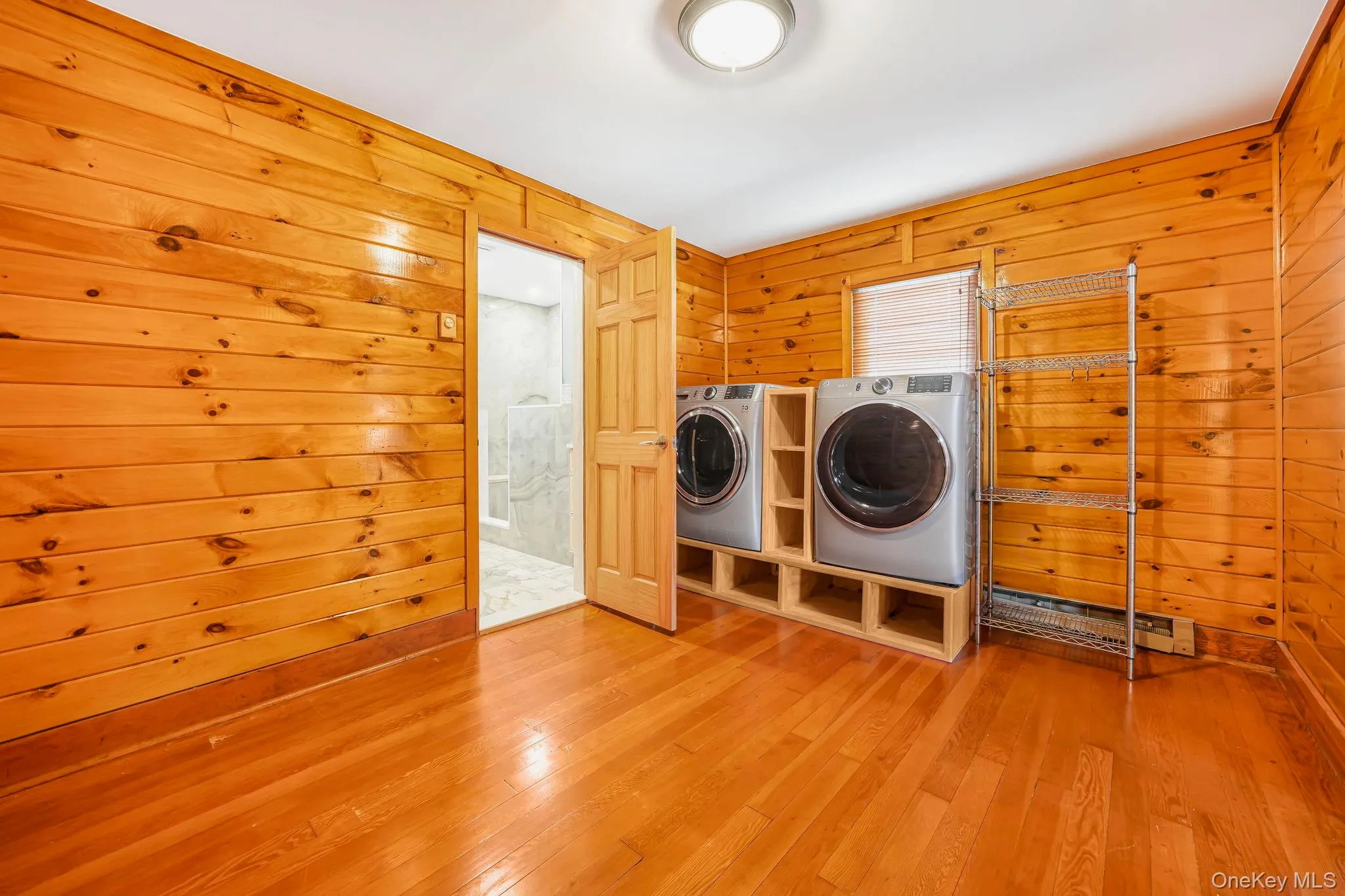 Laundry room featuring wood walls, wood-type flooring, separate washer and dryer, and a baseboard radiator Laundry room featuring wood walls, wood-type flooring, separate washer and dryer, and a baseboard radiator