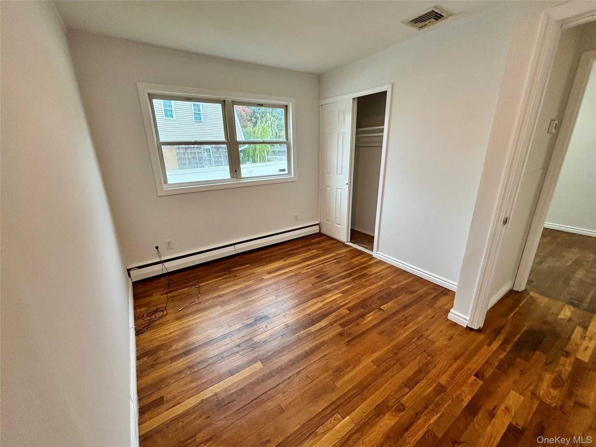 Unfurnished bedroom with a baseboard heating unit, dark wood finished floors, and a closet Unfurnished bedroom with a baseboard heating unit, dark wood finished floors, and a closet