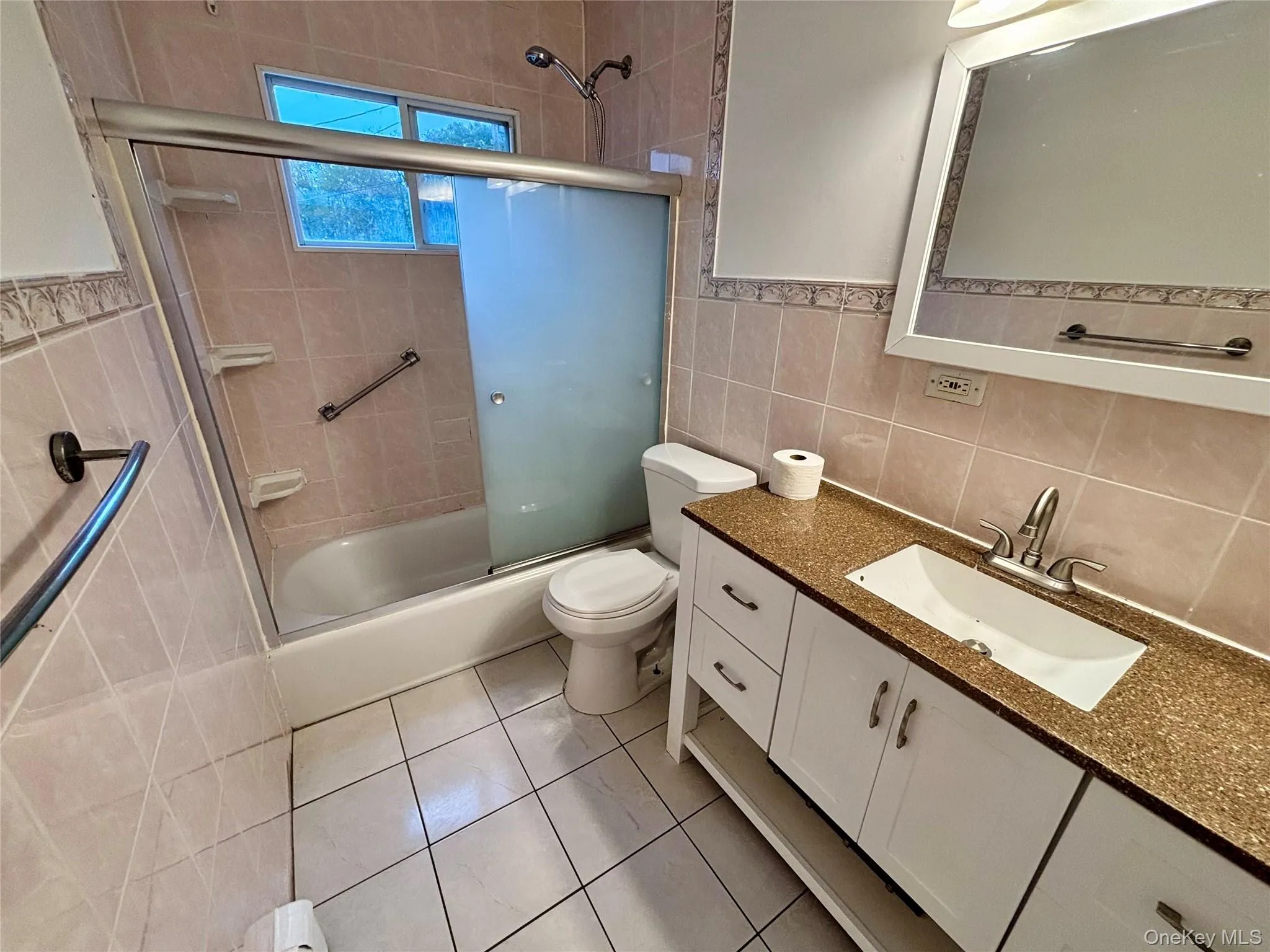 Bathroom featuring tile walls, vanity, shower / bath combination with glass door, light tile patterned floors, and tasteful backsplash Bathroom featuring tile walls, vanity, shower / bath combination with glass door, light tile patterned floors, and tasteful backsplash