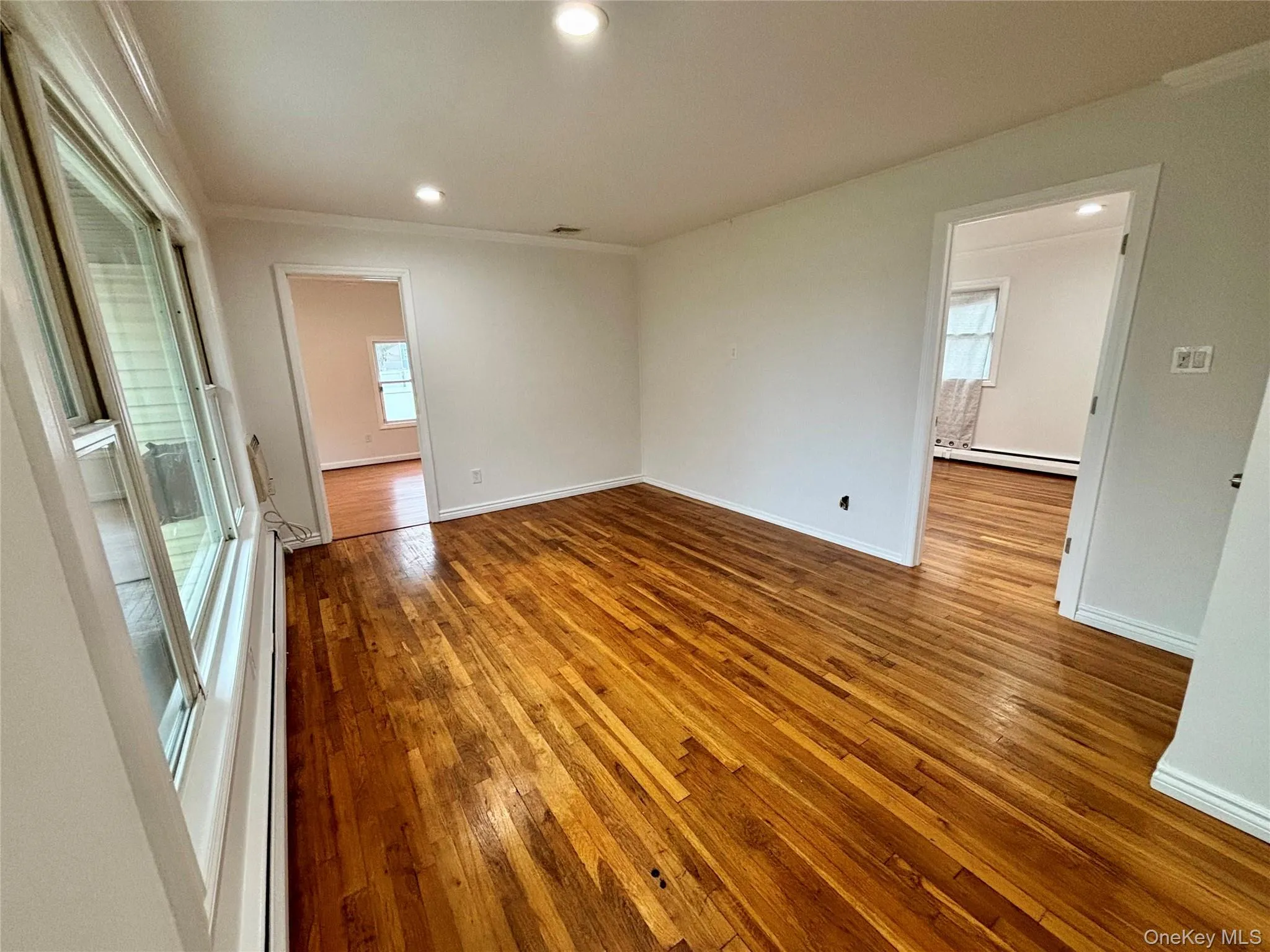 Empty room featuring wood-type flooring, recessed lighting, ornamental molding, and a baseboard heating unit Empty room featuring wood-type flooring, recessed lighting, ornamental molding, and a baseboard heating unit