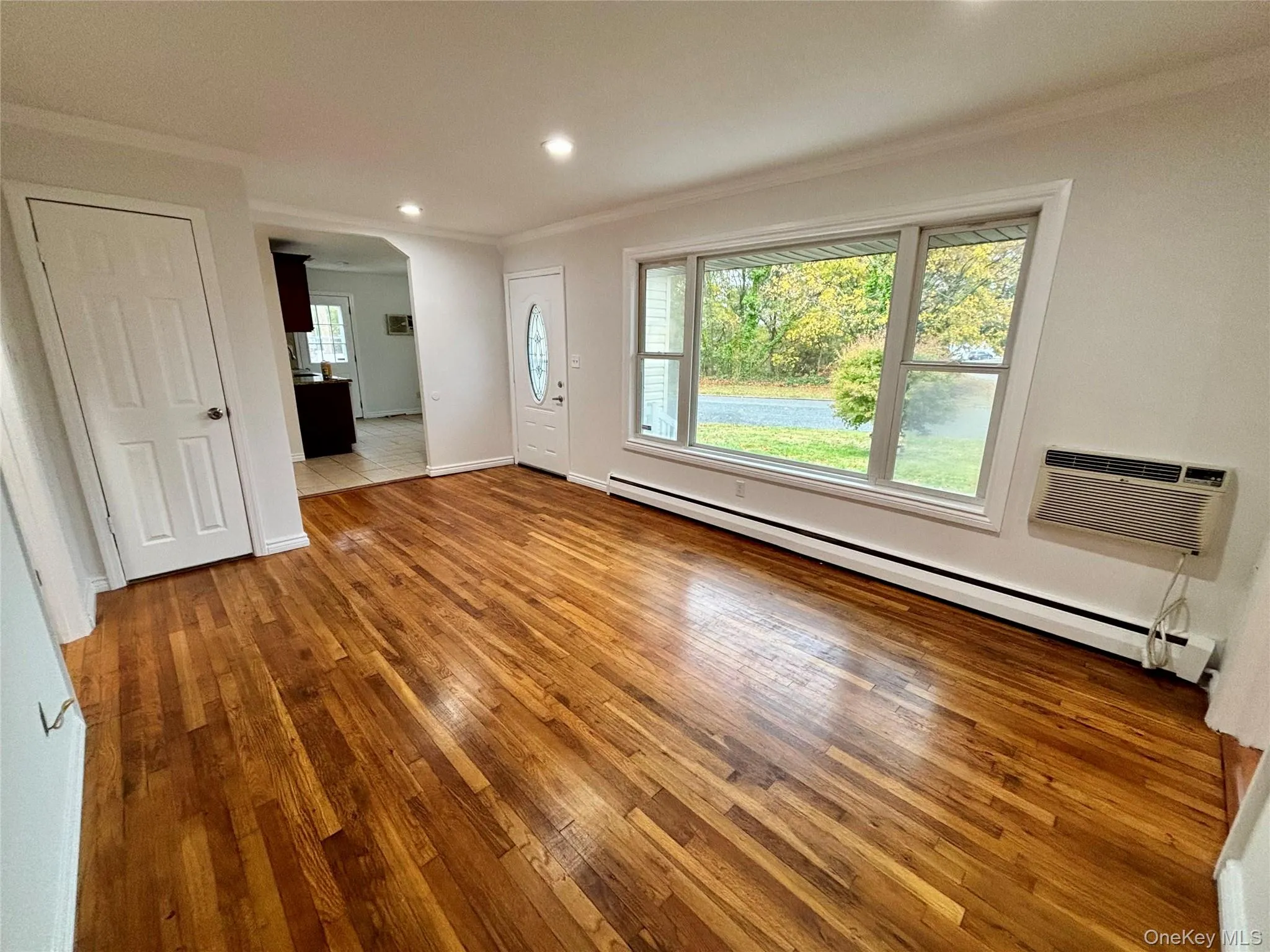 Unfurnished living room featuring ornamental molding, a baseboard heating unit, hardwood / wood-style flooring, a wall mounted AC, and recessed lighting Unfurnished living room featuring ornamental molding, a baseboard heating unit, hardwood / wood-style flooring, a wall mounted AC, and recessed lighting