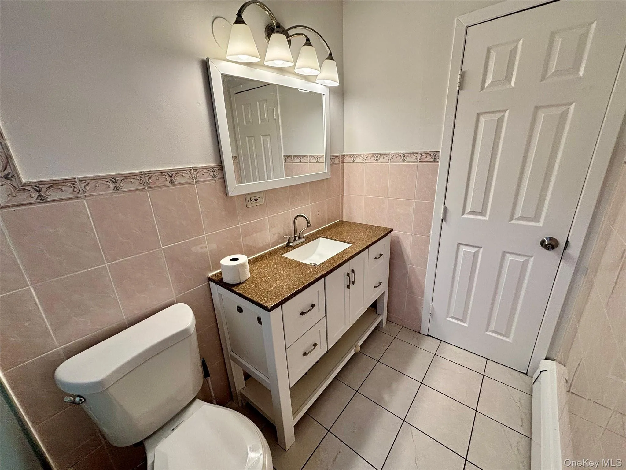 Half bathroom with tile walls, light tile patterned flooring, a wainscoted wall, vanity, and radiator heating unit Half bathroom with tile walls, light tile patterned flooring, a wainscoted wall, vanity, and radiator heating unit
