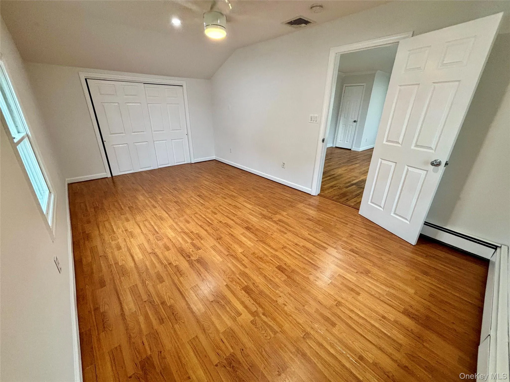Unfurnished bedroom featuring light wood-type flooring, a baseboard heating unit, lofted ceiling, a closet, and baseboard heating Unfurnished bedroom featuring light wood-type flooring, a baseboard heating unit, lofted ceiling, a closet, and baseboard heating