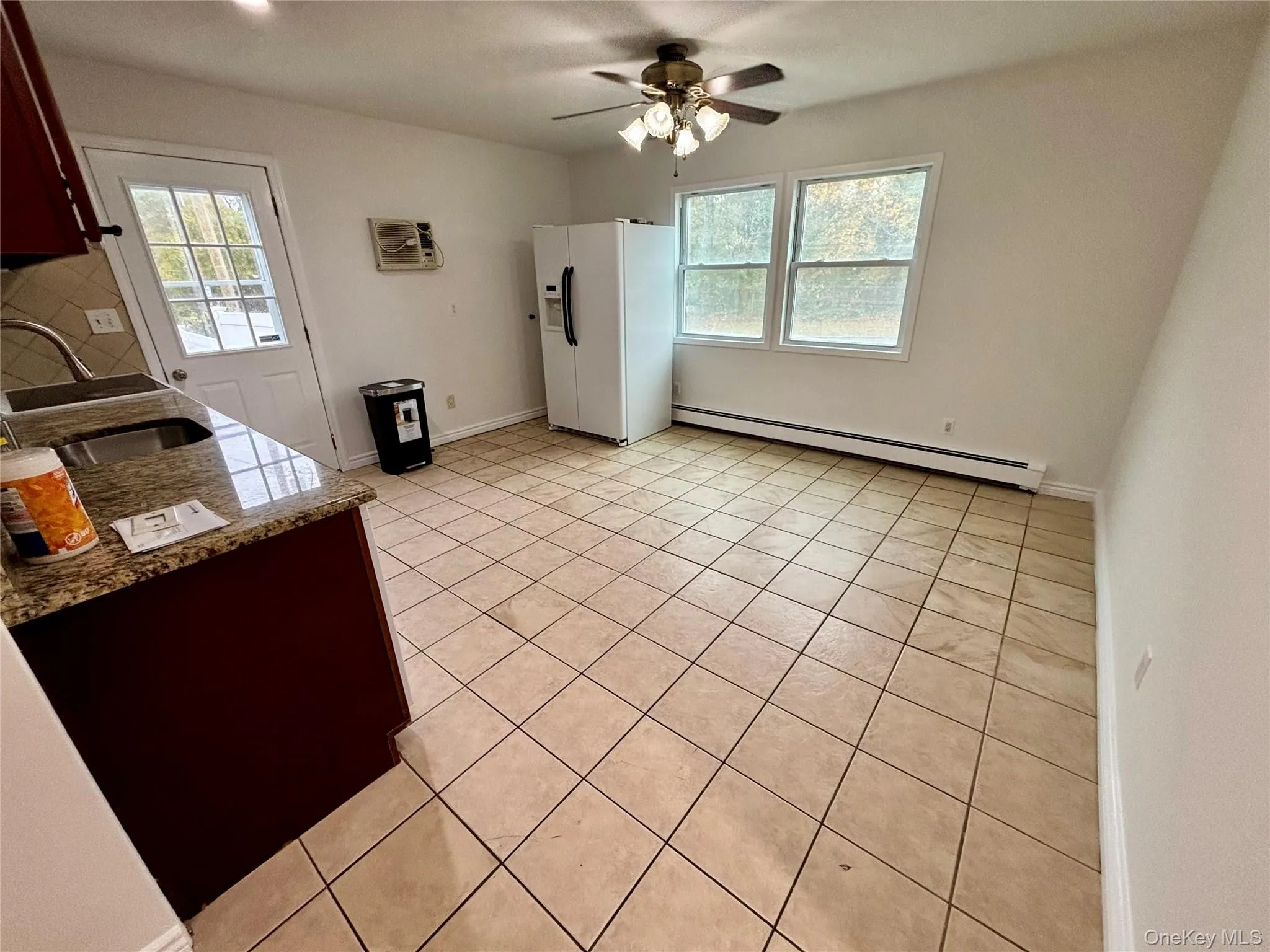 Kitchen featuring light tile patterned floors, white fridge with ice dispenser, a baseboard heating unit, light stone counters, and plenty of natural light Kitchen featuring light tile patterned floors, white fridge with ice dispenser, a baseboard heating unit, light stone counters, and plenty of natural light
