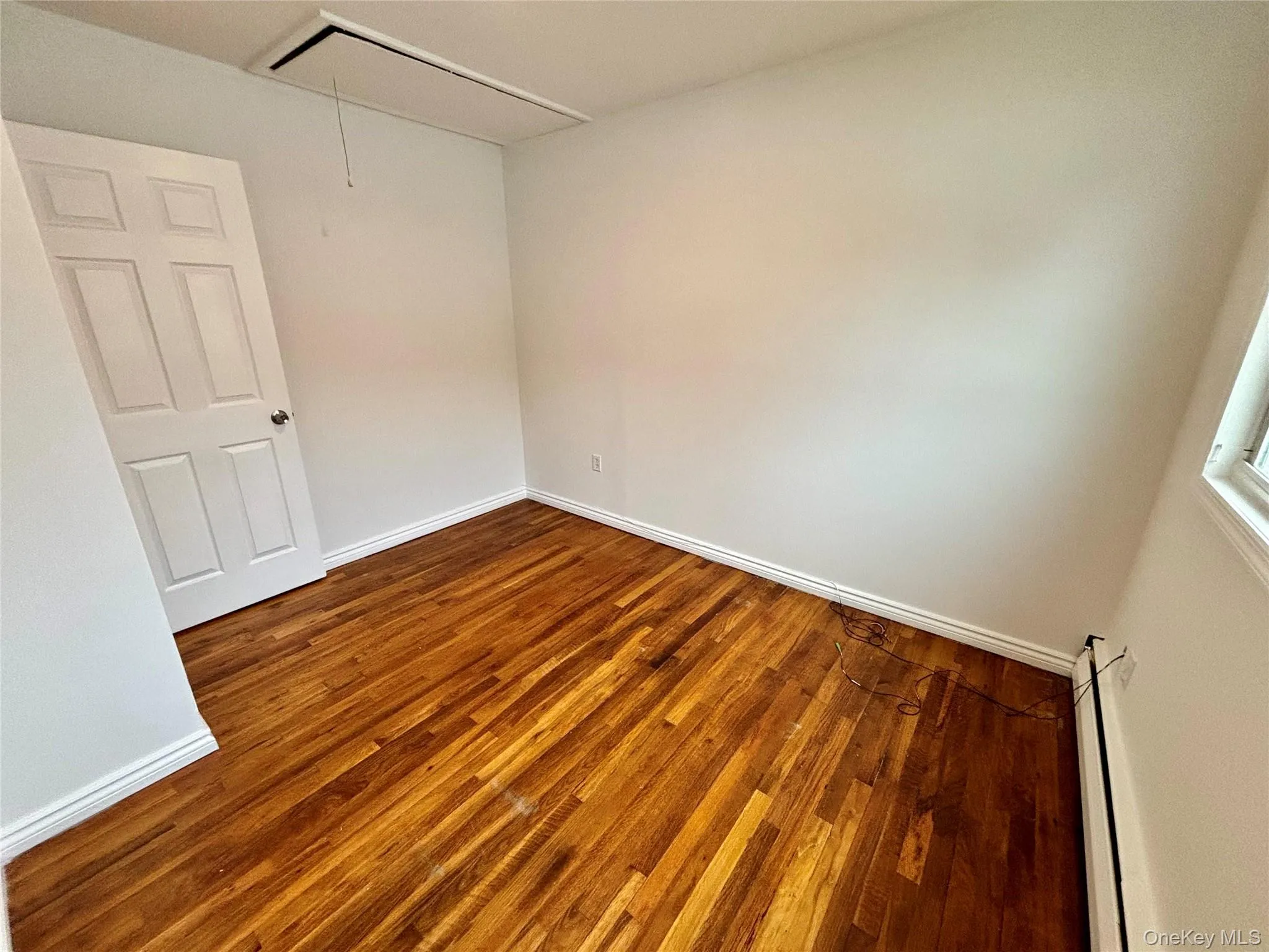 Unfurnished room with attic access, dark wood-type flooring, and a baseboard heating unit Unfurnished room with attic access, dark wood-type flooring, and a baseboard heating unit