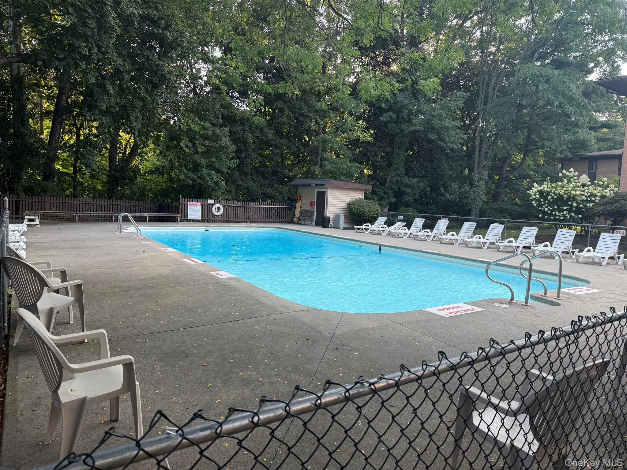 Community pool with a patio area, an outbuilding, and view of wooded area Community pool with a patio area, an outbuilding, and view of wooded area