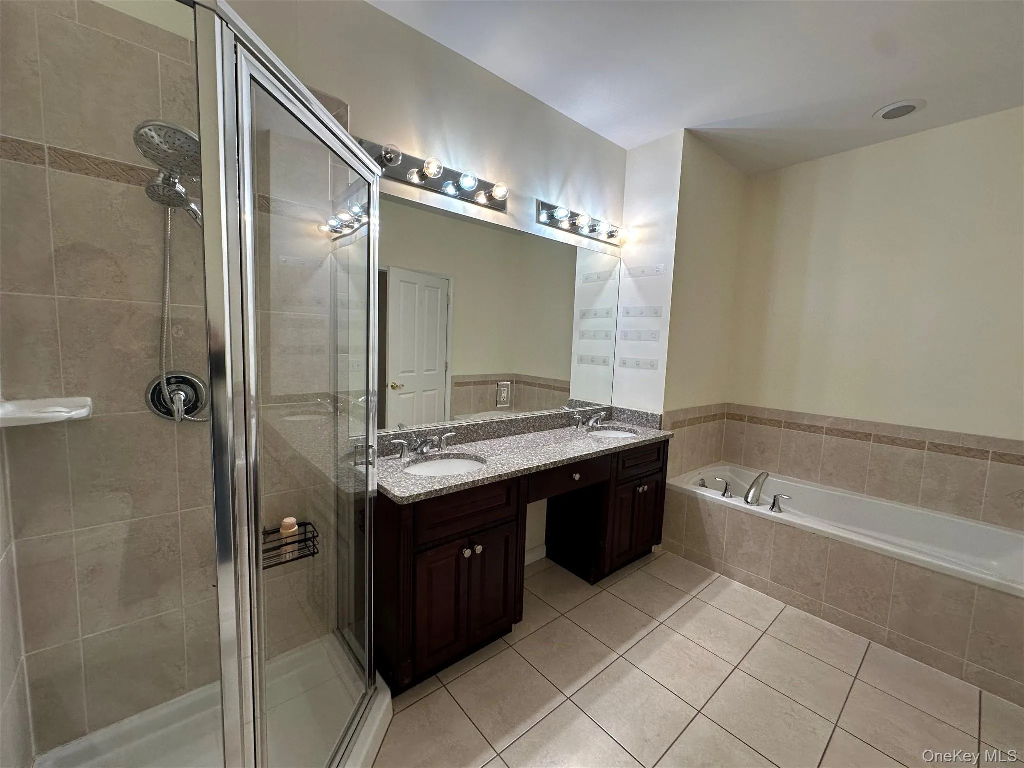 Full bathroom with double vanity, light tile patterned flooring, a stall shower, and a garden tub Full bathroom with double vanity, light tile patterned flooring, a stall shower, and a garden tub