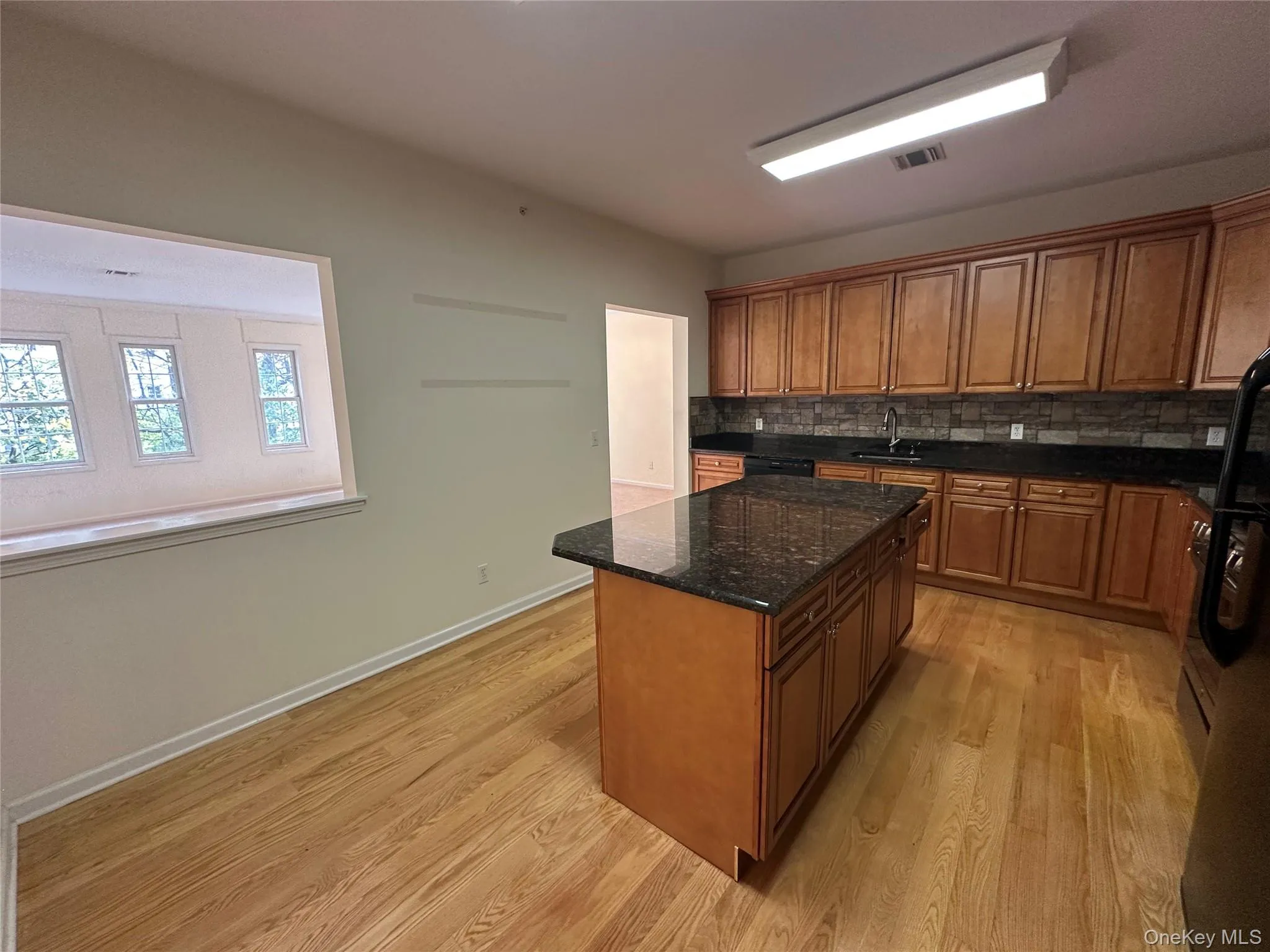 Kitchen with dark stone counters, backsplash, brown cabinets, and light wood-style floors Kitchen with dark stone counters, backsplash, brown cabinets, and light wood-style floors