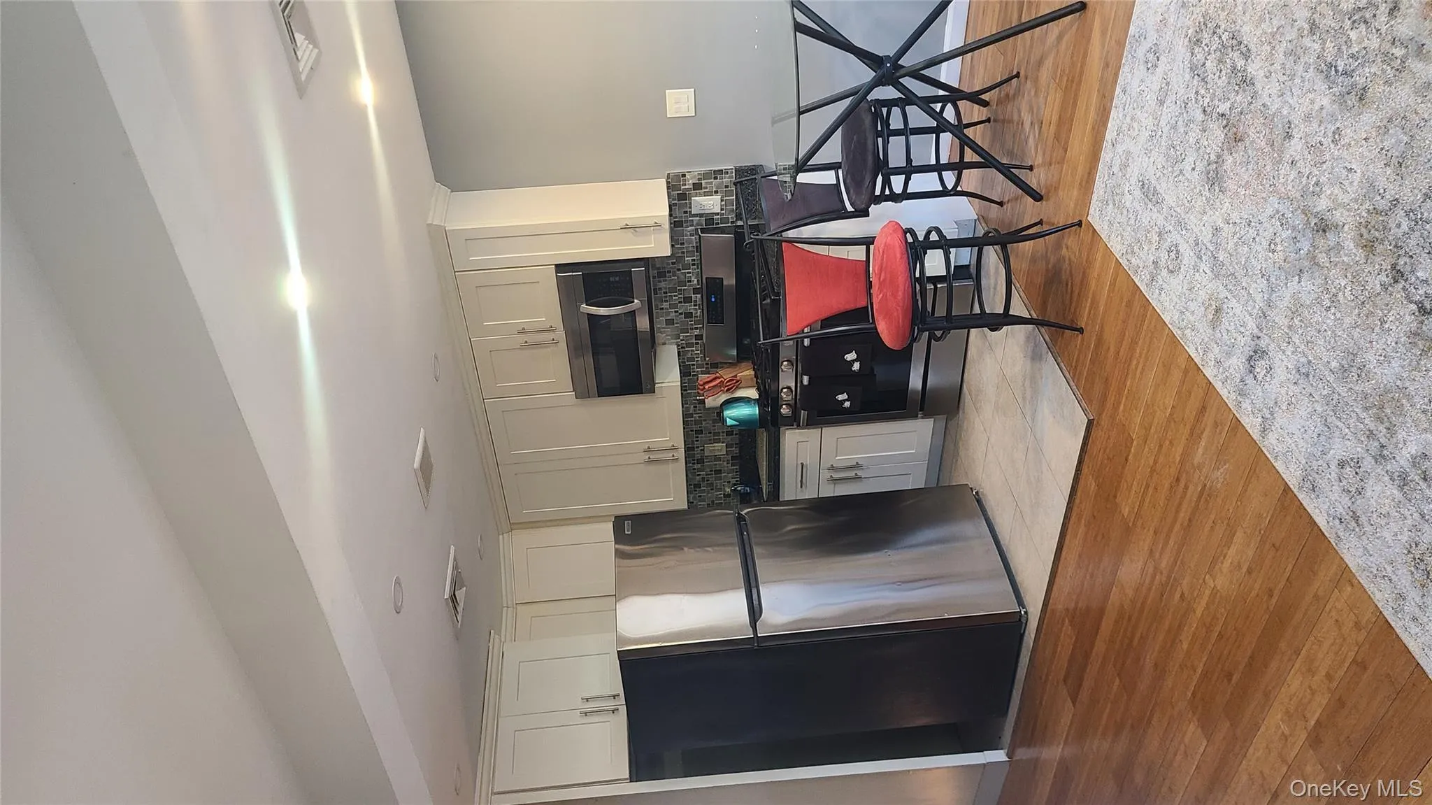 Kitchen with stainless steel appliances, decorative backsplash, light wood-style flooring, dark countertops, and white cabinets Kitchen with stainless steel appliances, decorative backsplash, light wood-style flooring, dark countertops, and white cabinets