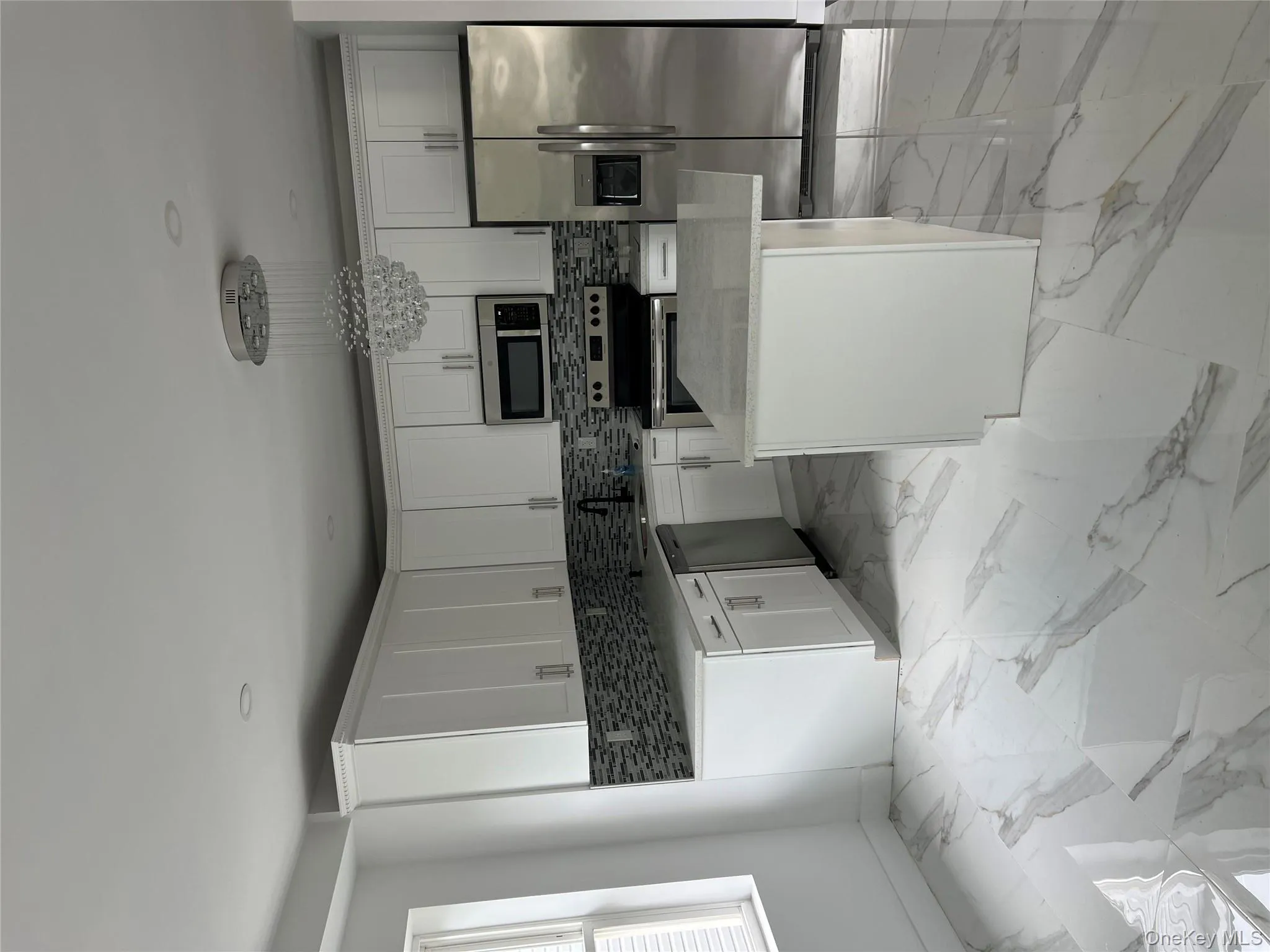 Kitchen with light marble finish floors, backsplash, appliances with stainless steel finishes, white cabinets, and light stone counters Kitchen with light marble finish floors, backsplash, appliances with stainless steel finishes, white cabinets, and light stone counters