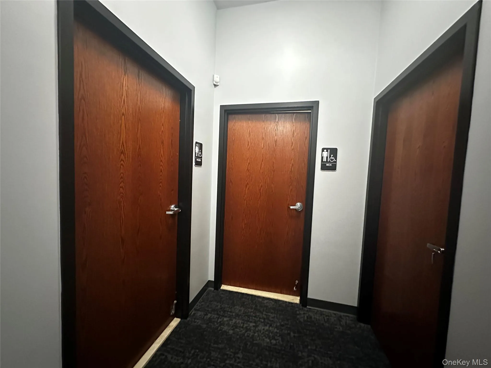Corridor featuring dark carpet and baseboards Corridor featuring dark carpet and baseboards