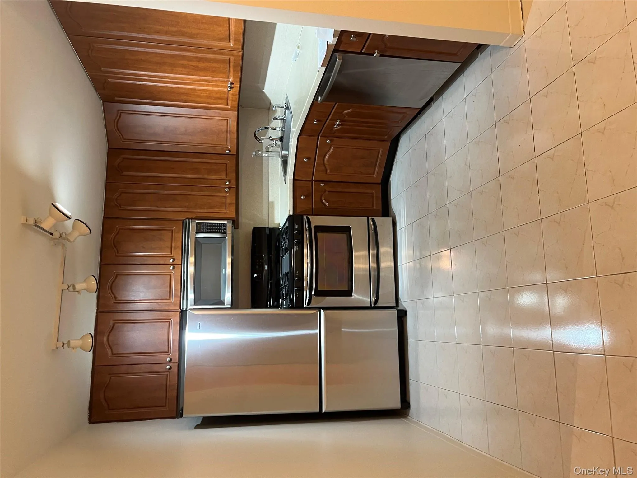 Kitchen featuring stainless steel appliances, light countertops, light tile patterned floors, and track lighting Kitchen featuring stainless steel appliances, light countertops, light tile patterned floors, and track lighting