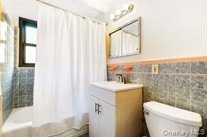 Bathroom with shower / bath combo, tile walls, vanity, and wainscoting Bathroom with shower / bath combo, tile walls, vanity, and wainscoting