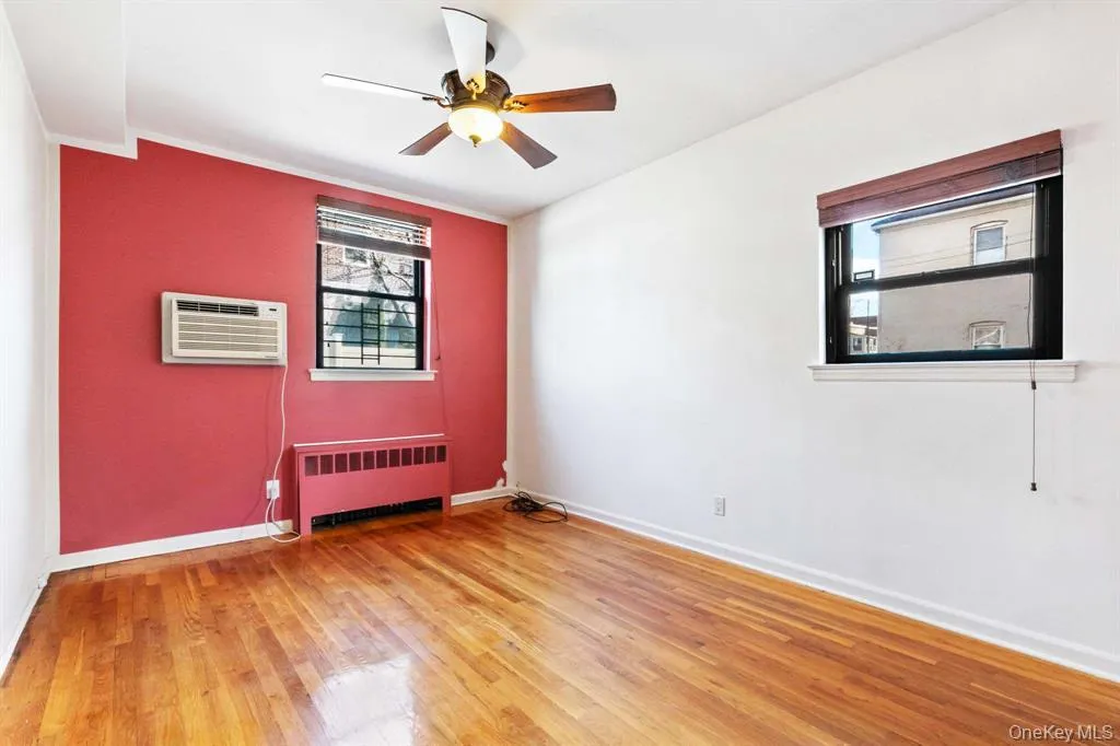 Unfurnished room with radiator, light wood-style flooring, ceiling fan, a wall mounted AC, and ornamental molding Unfurnished room with radiator, light wood-style flooring, ceiling fan, a wall mounted AC, and ornamental molding