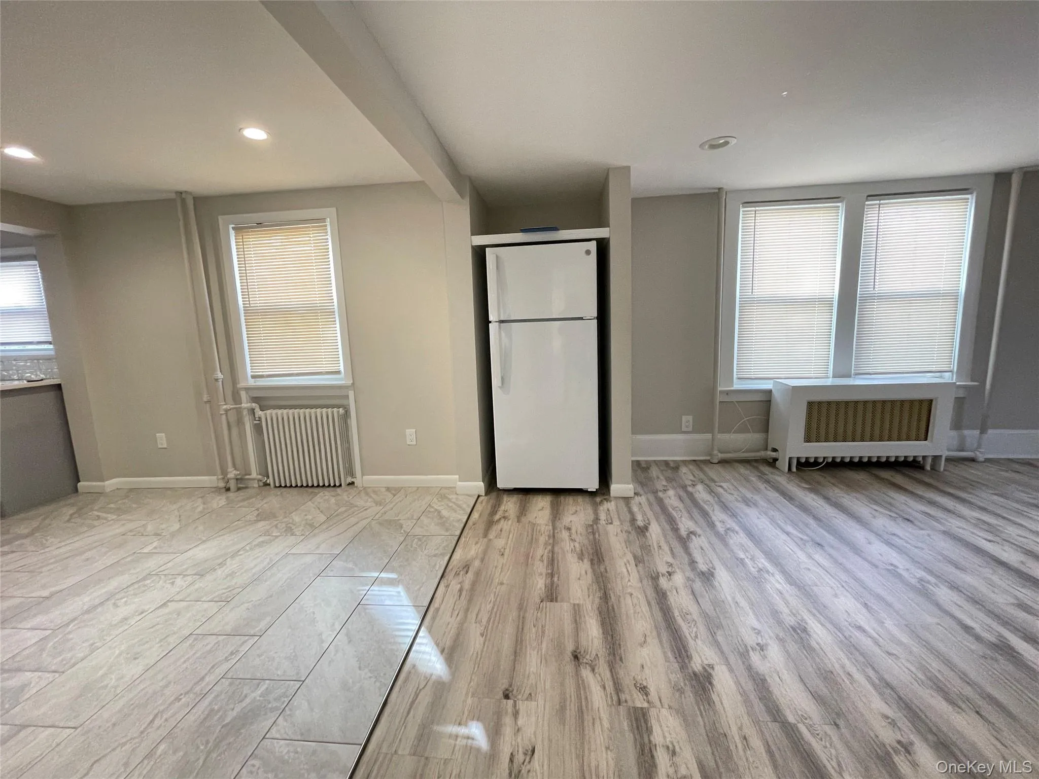 Unfurnished bedroom featuring freestanding refrigerator, light wood finished floors, radiator heating unit, and recessed lighting Unfurnished bedroom featuring freestanding refrigerator, light wood finished floors, radiator heating unit, and recessed lighting
