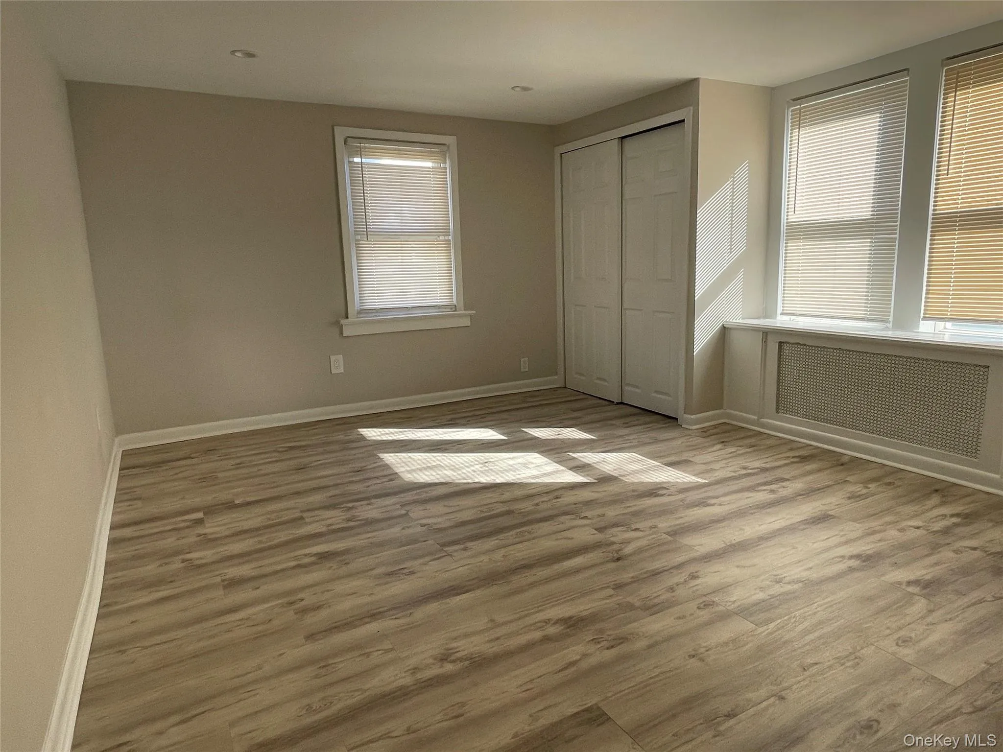 Unfurnished bedroom with light wood-style flooring, radiator heating unit, and a closet Unfurnished bedroom with light wood-style flooring, radiator heating unit, and a closet