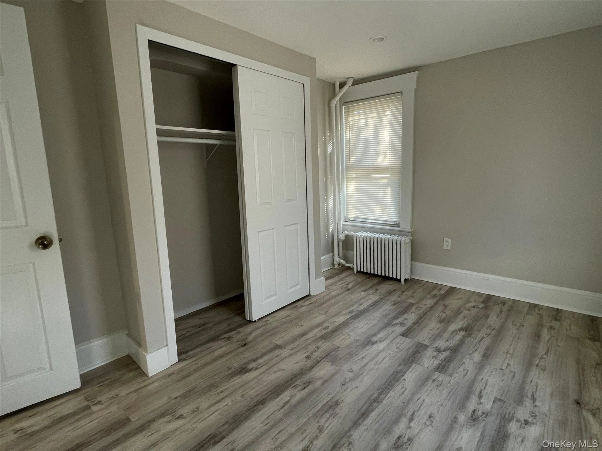 Unfurnished bedroom with radiator heating unit, light wood-type flooring, and a closet Unfurnished bedroom with radiator heating unit, light wood-type flooring, and a closet