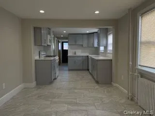 Kitchen featuring gray cabinets, radiator, tasteful backsplash, gas range gas stove, and light countertops Kitchen featuring gray cabinets, radiator, tasteful backsplash, gas range gas stove, and light countertops