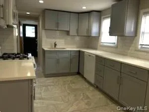 Kitchen with gray cabinets, light countertops, recessed lighting, tasteful backsplash, and dishwashing machine Kitchen with gray cabinets, light countertops, recessed lighting, tasteful backsplash, and dishwashing machine