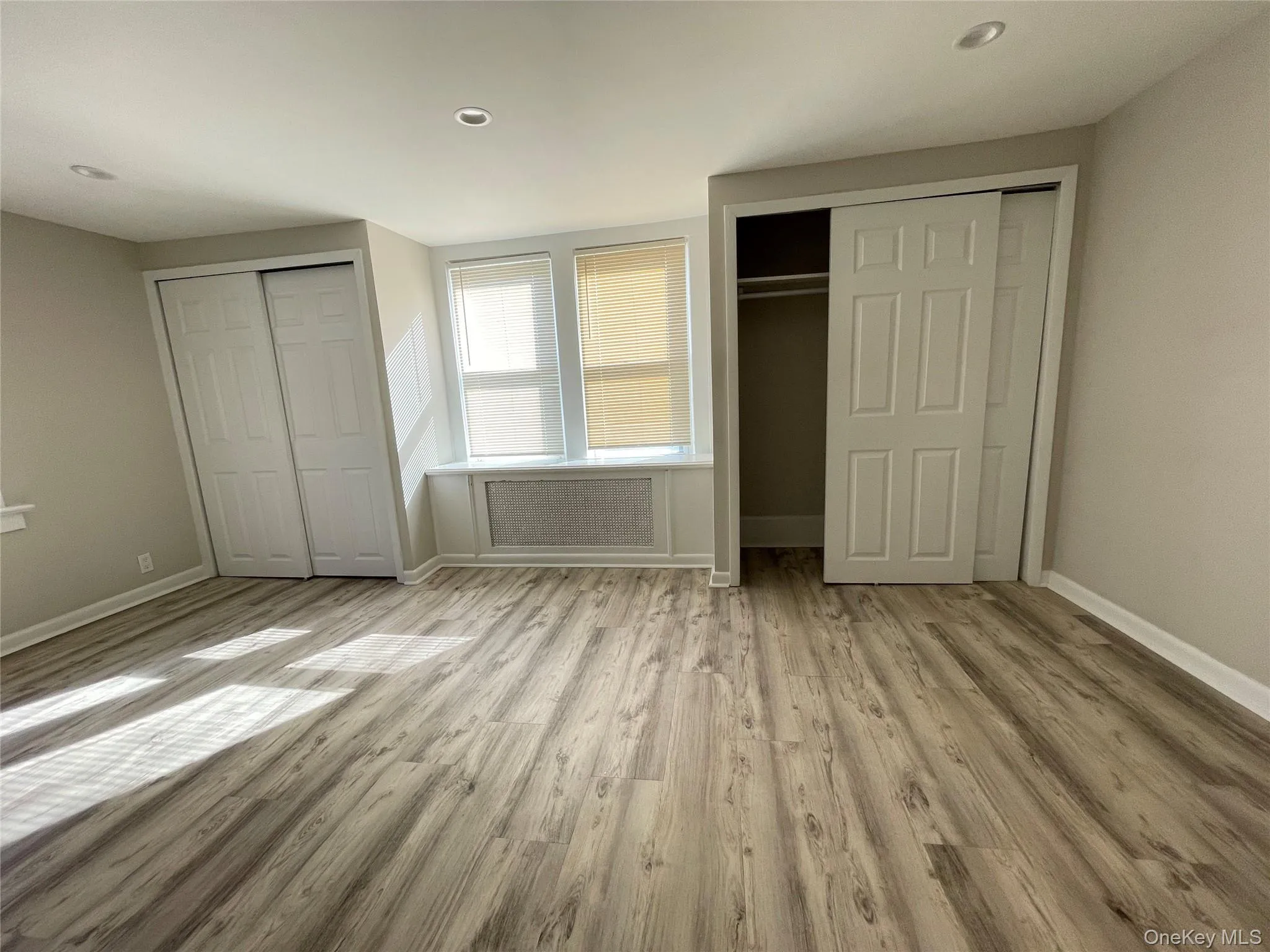 Unfurnished bedroom featuring two closets, light wood-style flooring, recessed lighting, and radiator Unfurnished bedroom featuring two closets, light wood-style flooring, recessed lighting, and radiator