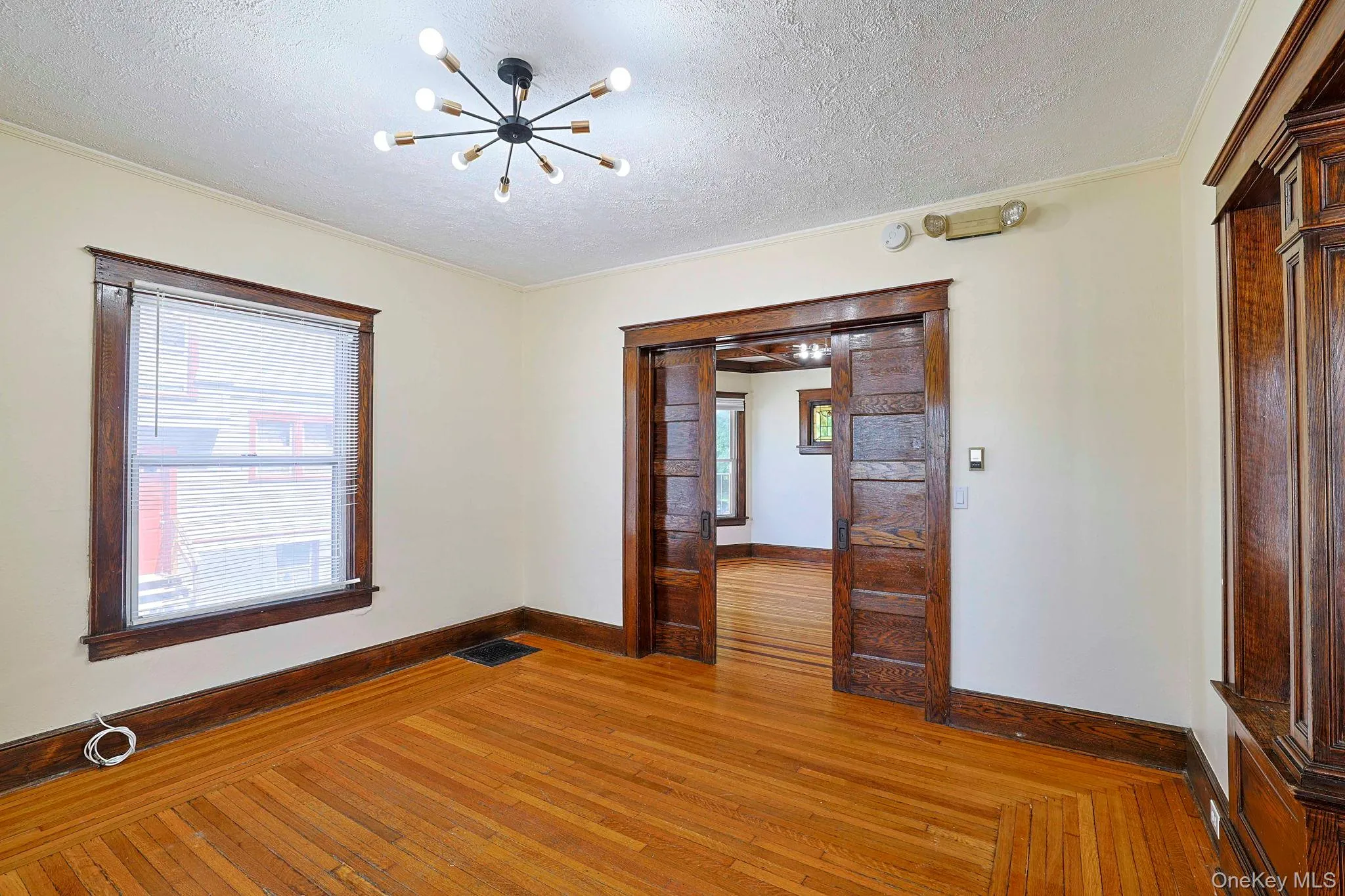 Spare room featuring hardwood / wood-style floors, plenty of natural light, a textured ceiling, a chandelier, and crown molding Spare room featuring hardwood / wood-style floors, plenty of natural light, a textured ceiling, a chandelier, and crown molding