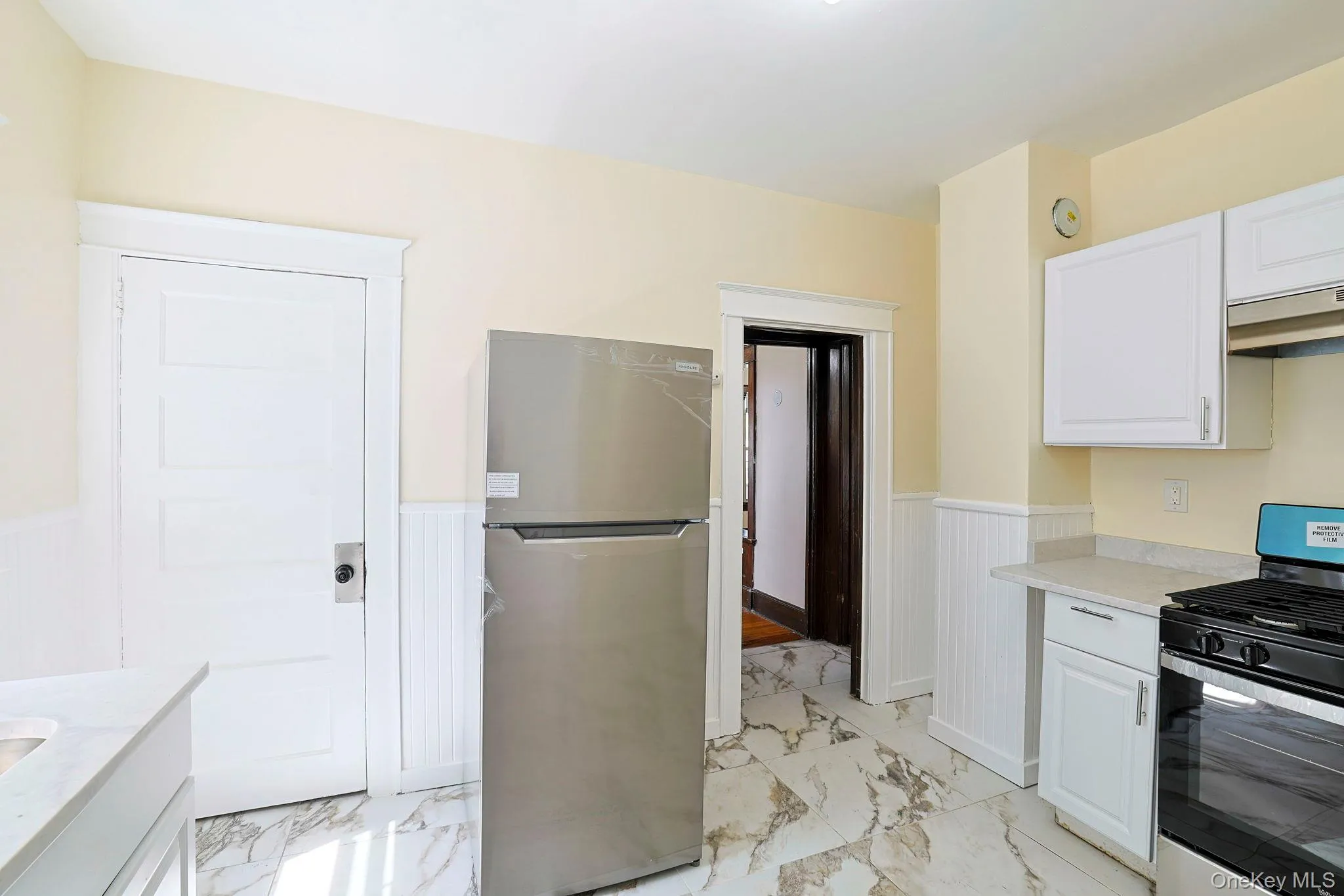 Kitchen with appliances with stainless steel finishes, white cabinets, a wainscoted wall, light marble finish floors, and light stone countertops Kitchen with appliances with stainless steel finishes, white cabinets, a wainscoted wall, light marble finish floors, and light stone countertops