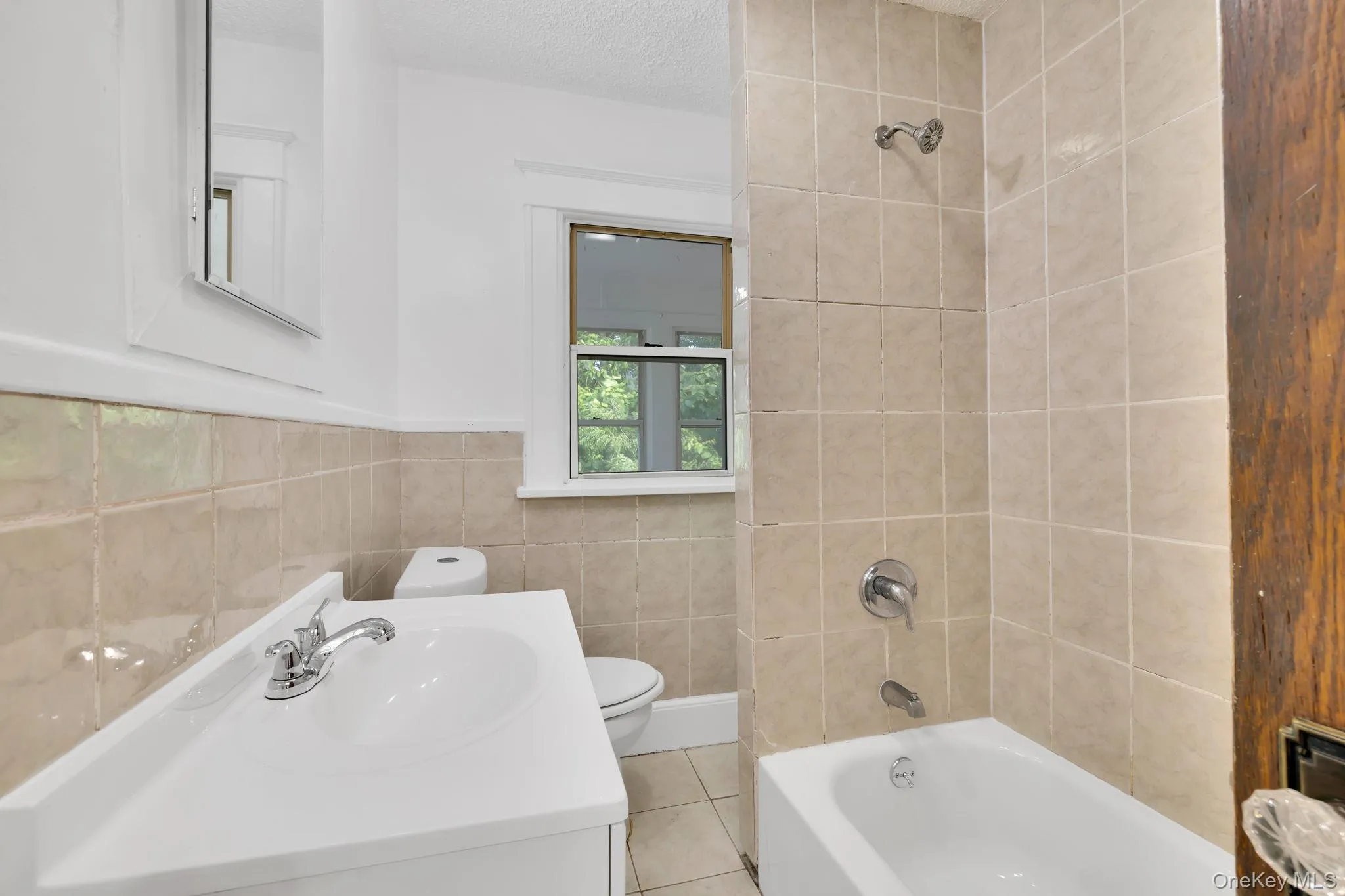Bathroom featuring shower combination, vanity, tile walls, a textured ceiling, and tile patterned flooring Bathroom featuring shower combination, vanity, tile walls, a textured ceiling, and tile patterned flooring