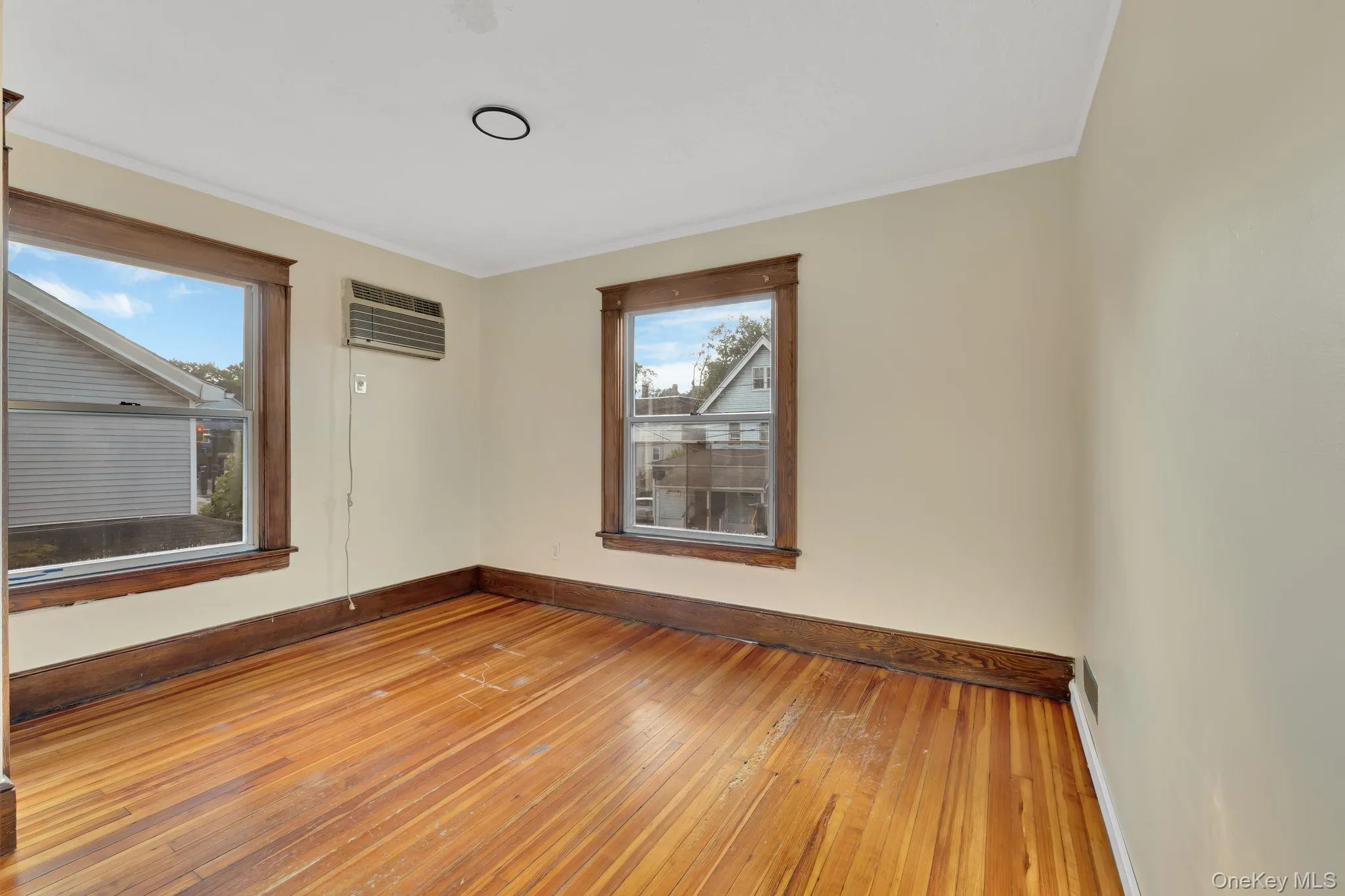 Empty room with wood-type flooring, plenty of natural light, an AC wall unit, and crown molding Empty room with wood-type flooring, plenty of natural light, an AC wall unit, and crown molding