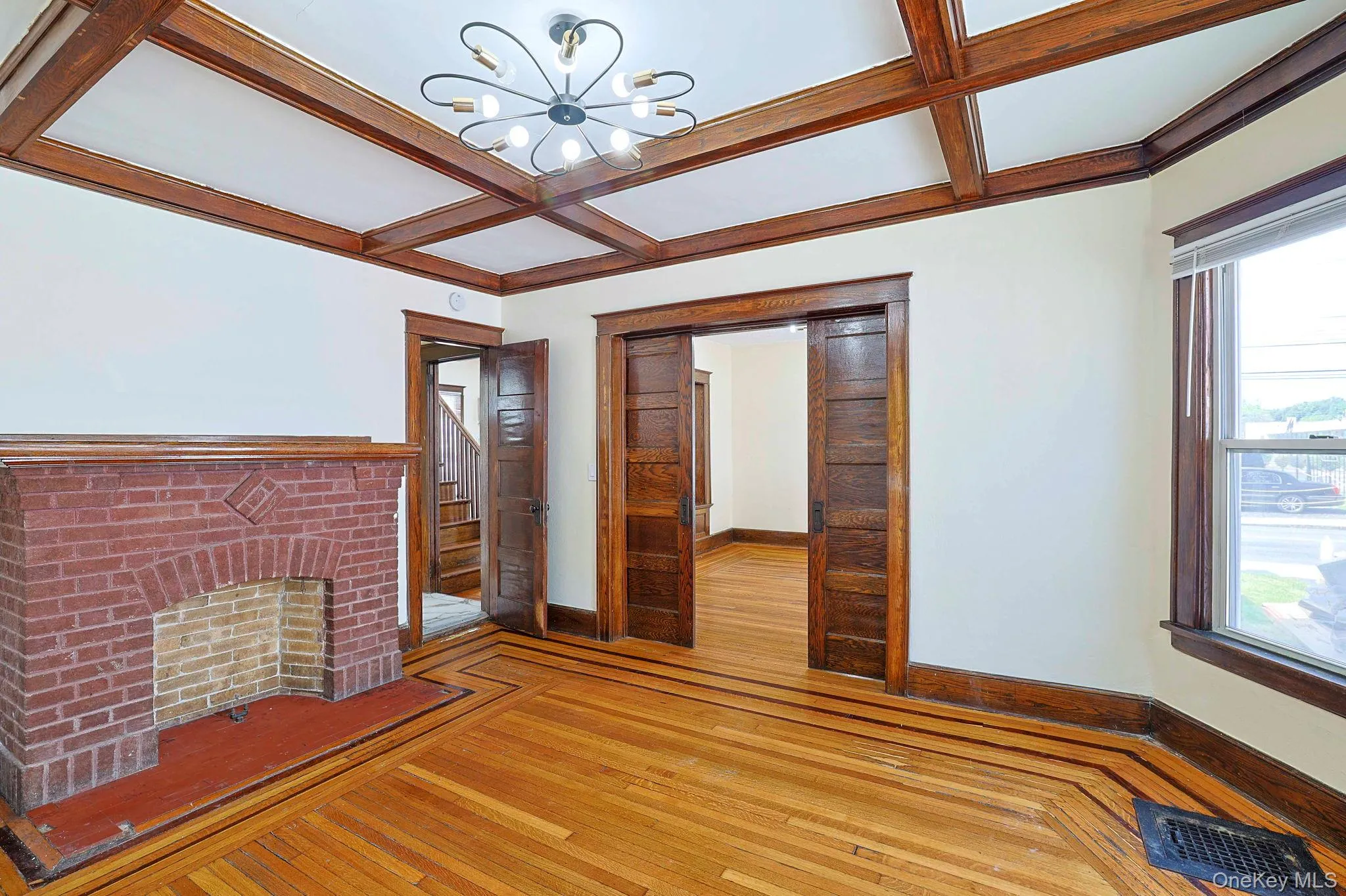Unfurnished living room featuring coffered ceiling, hardwood / wood-style floors, beam ceiling, a chandelier, and a brick fireplace Unfurnished living room featuring coffered ceiling, hardwood / wood-style floors, beam ceiling, a chandelier, and a brick fireplace