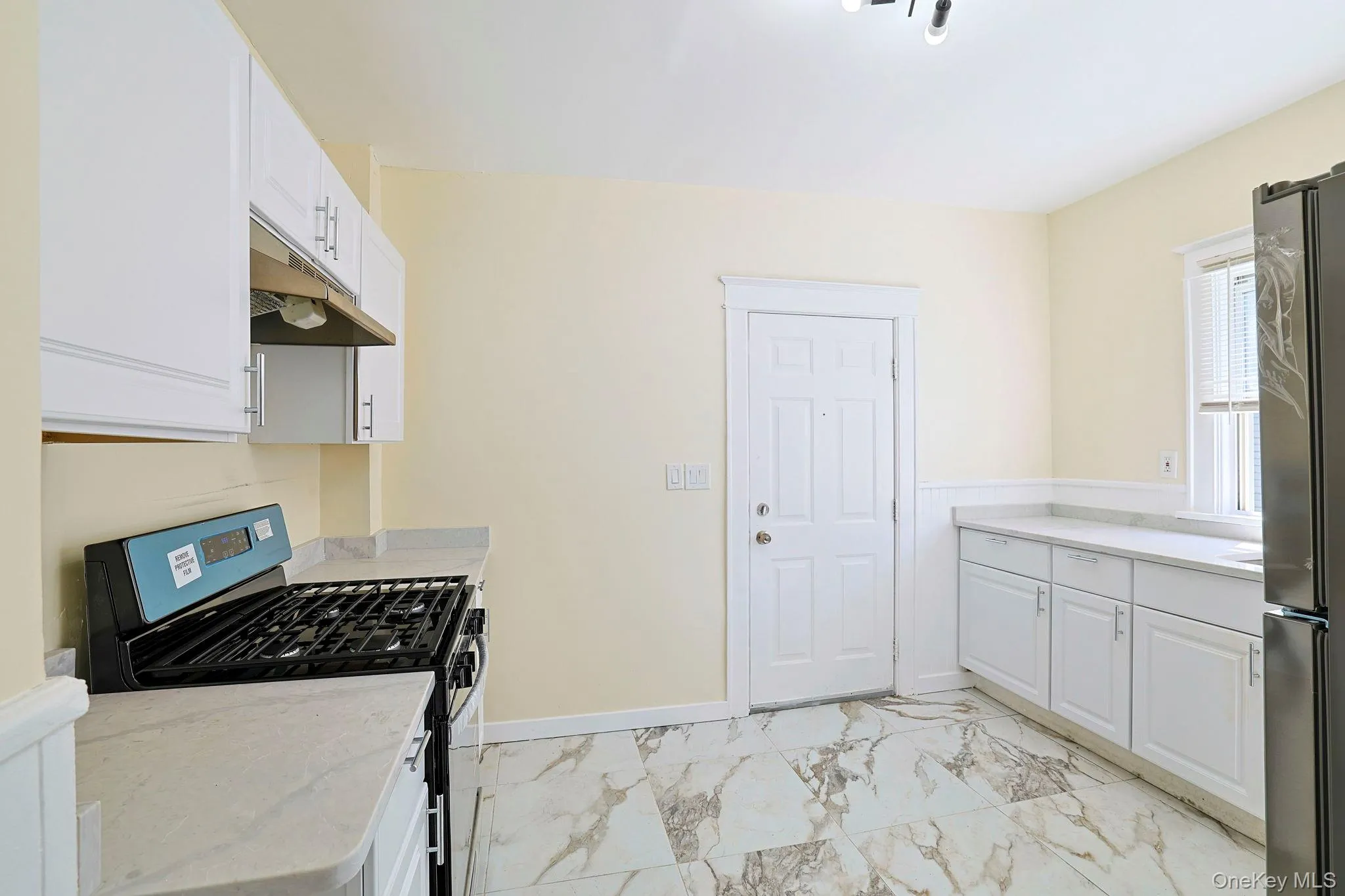 Kitchen with appliances with stainless steel finishes, white cabinets, light marble finish flooring, and under cabinet range hood Kitchen with appliances with stainless steel finishes, white cabinets, light marble finish flooring, and under cabinet range hood