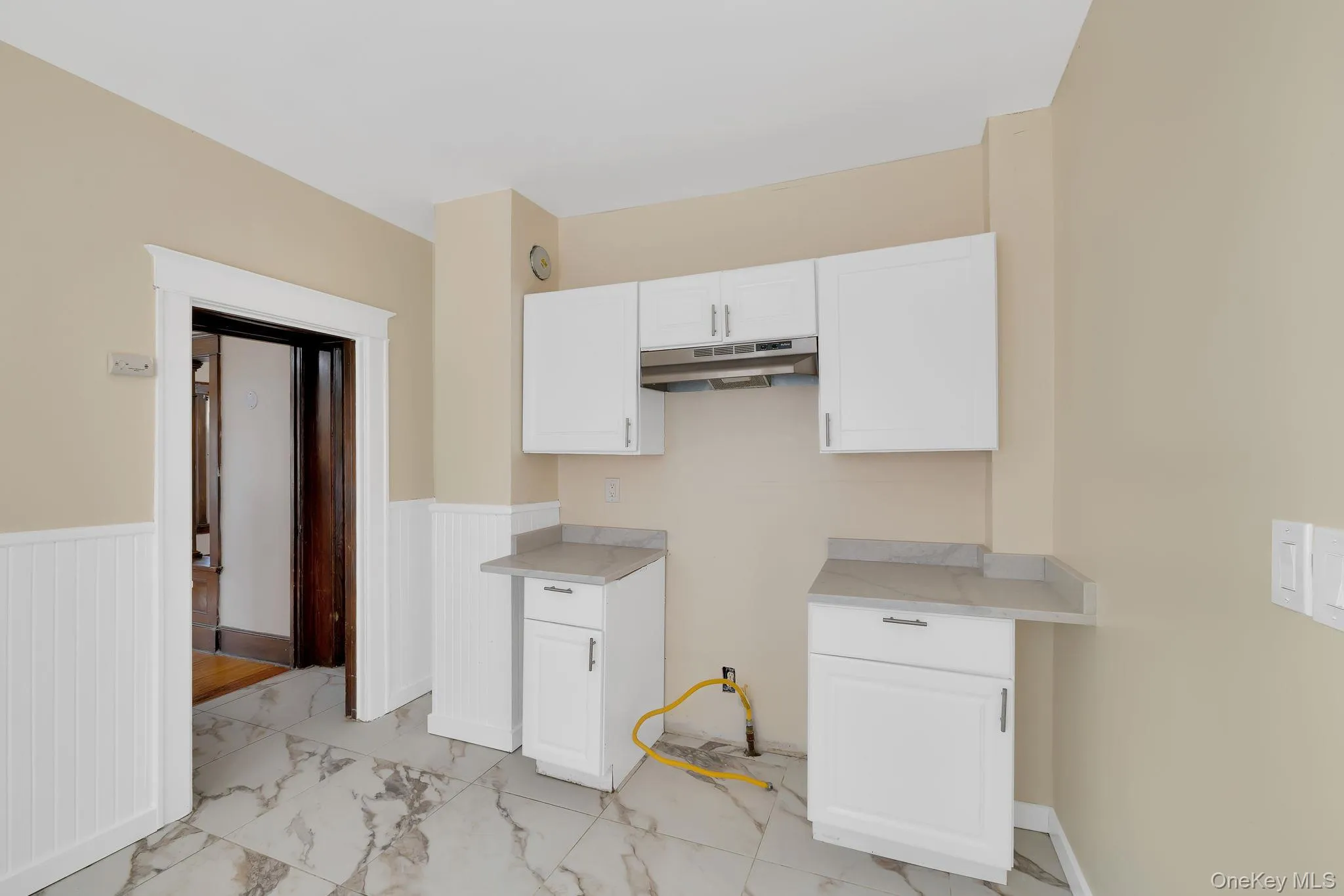 Kitchen with light countertops, white cabinets, light marble finish flooring, under cabinet range hood, and wainscoting Kitchen with light countertops, white cabinets, light marble finish flooring, under cabinet range hood, and wainscoting