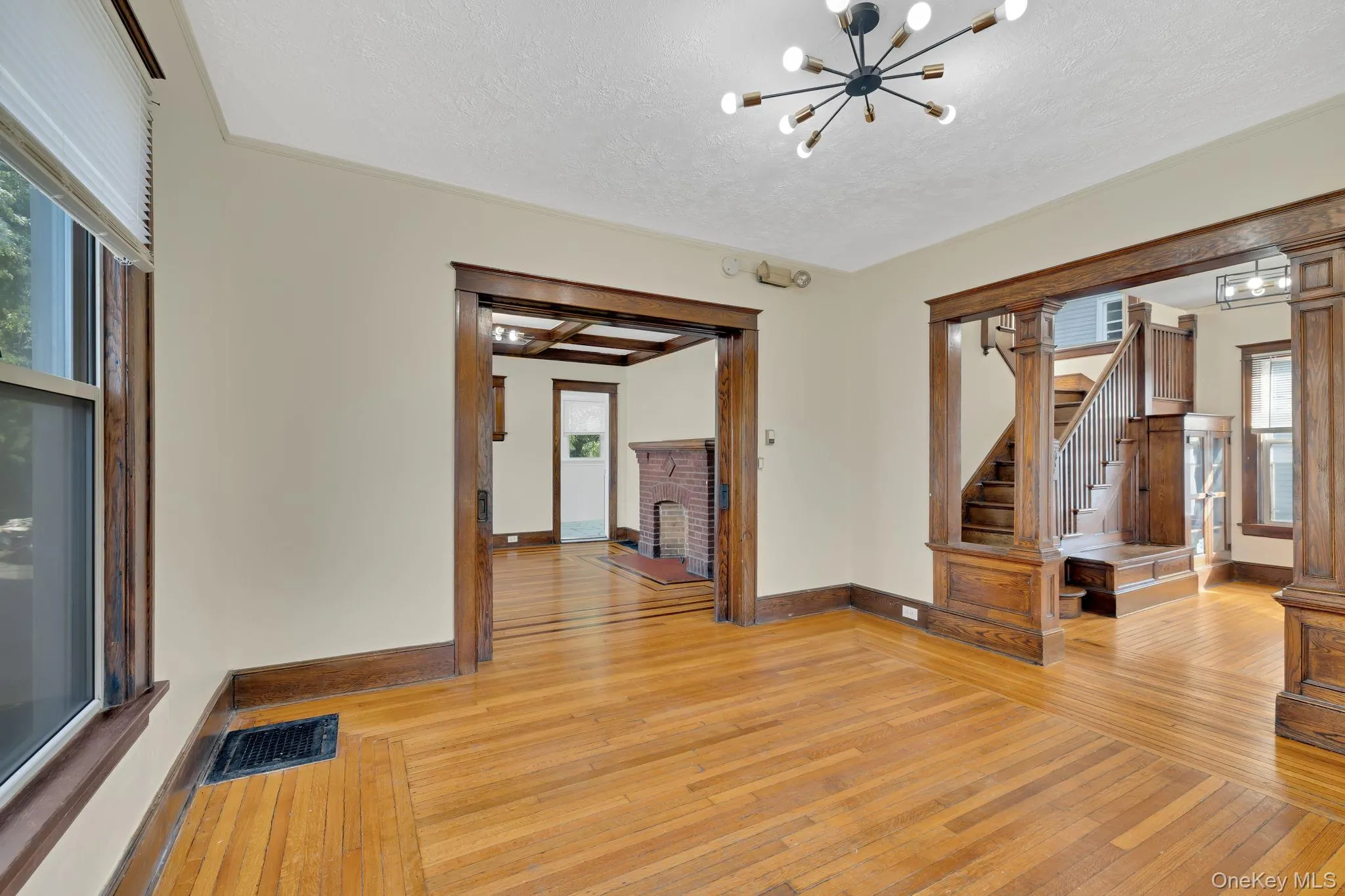 Unfurnished living room with light wood finished floors, a chandelier, a fireplace, stairway, and a textured ceiling Unfurnished living room with light wood finished floors, a chandelier, a fireplace, stairway, and a textured ceiling